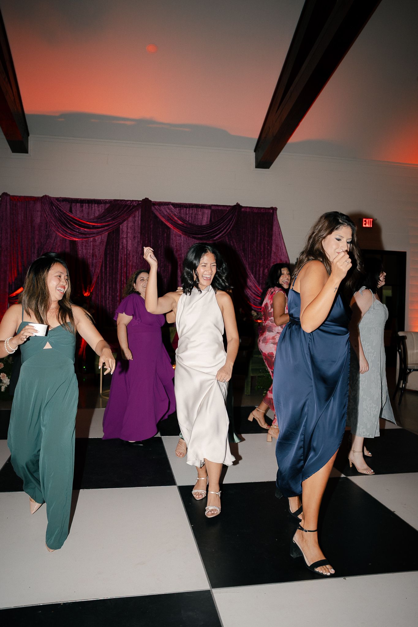 People dancing and having fun at a lively wedding reception party with purple decor in the background.