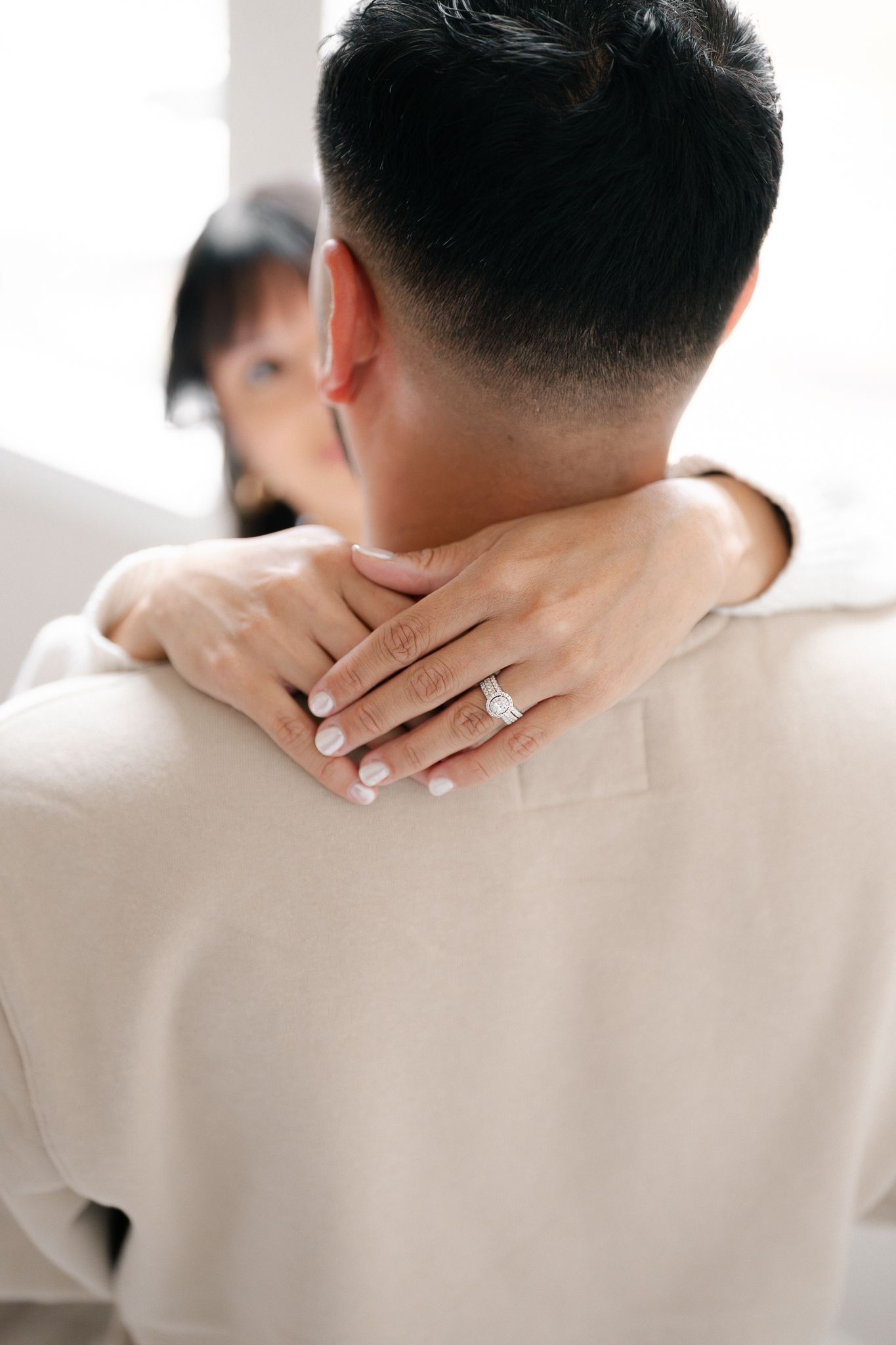A hand with an engagement ring rests on someone's shoulder in a tender romantic moment.