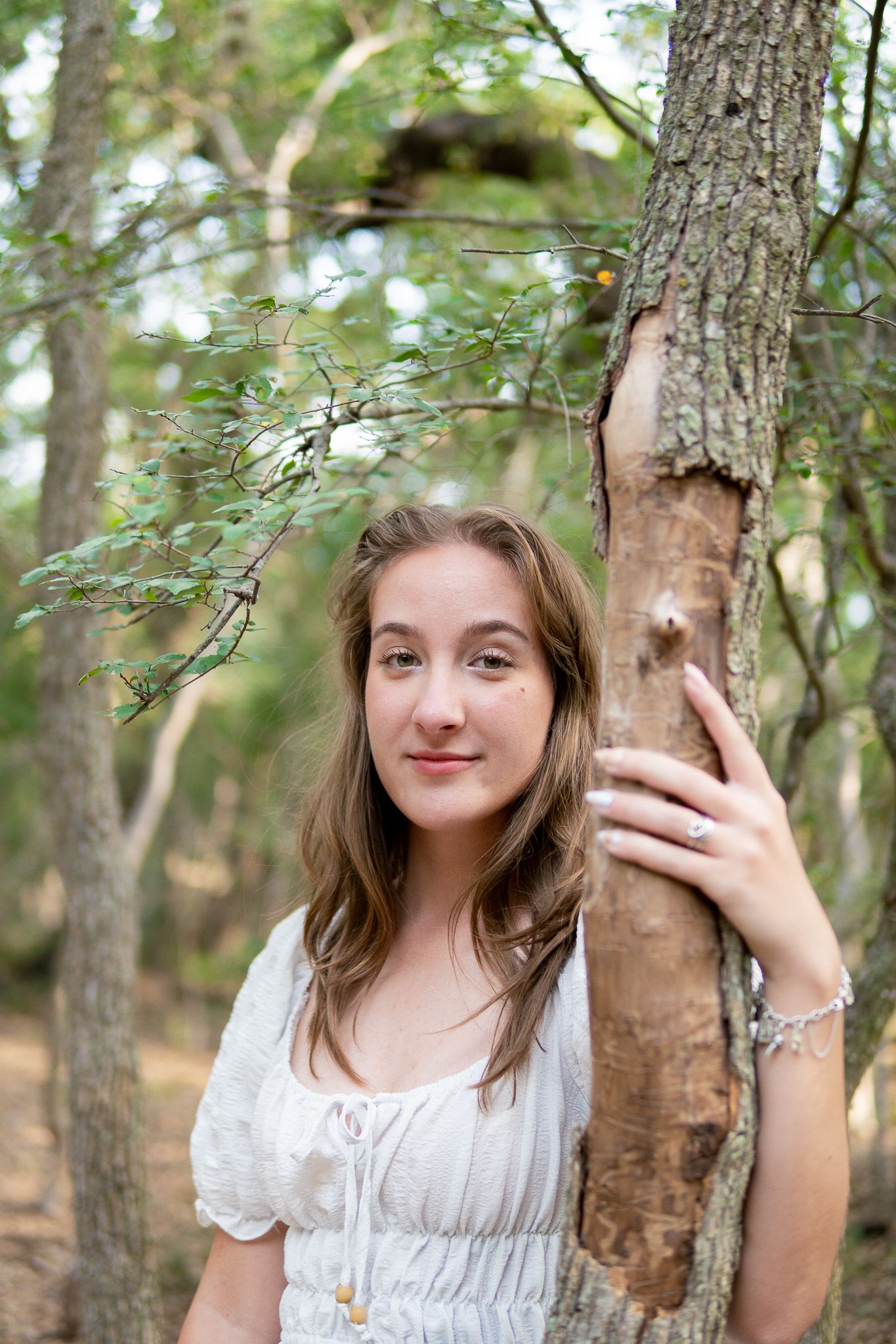 A series of candid photos in a forest setting shows someone in a white dress posing playfully next to tree trunks.