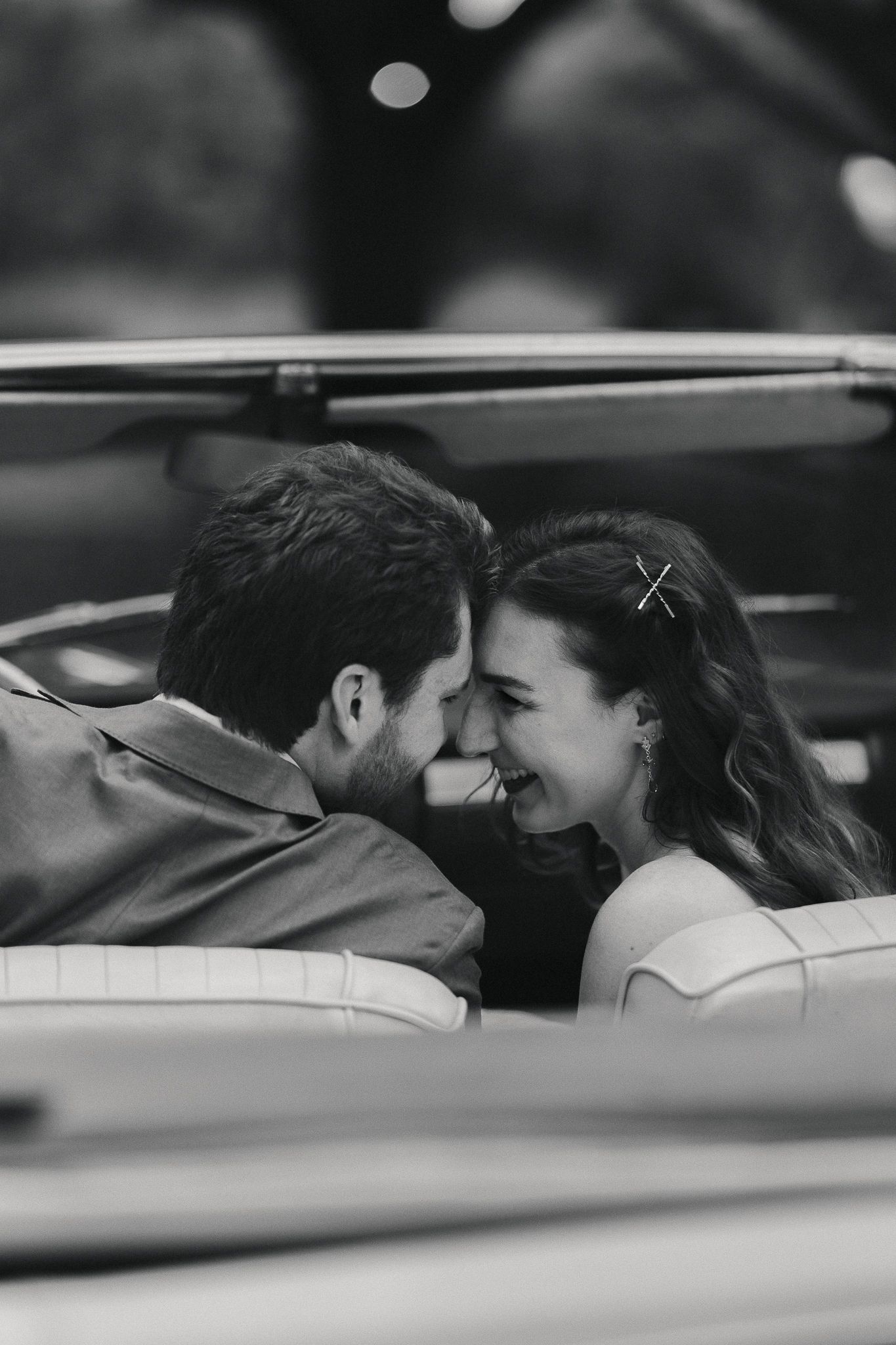 Black and white photo of a smiling couple leaning close together in a vintage convertible car.