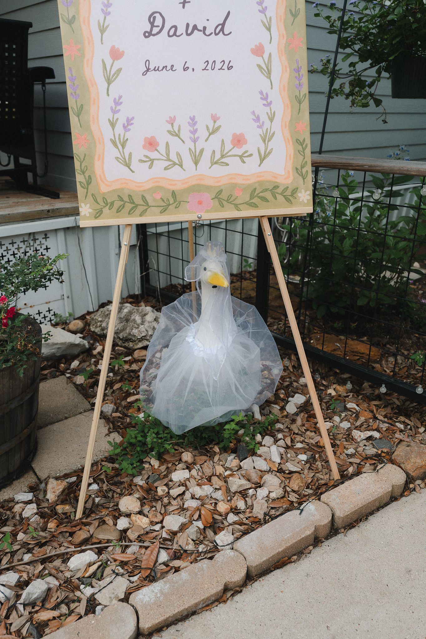 A decorative goose statue wearing a bridal veil beside a floral wedding welcome sign for David dated June 6, 2026.