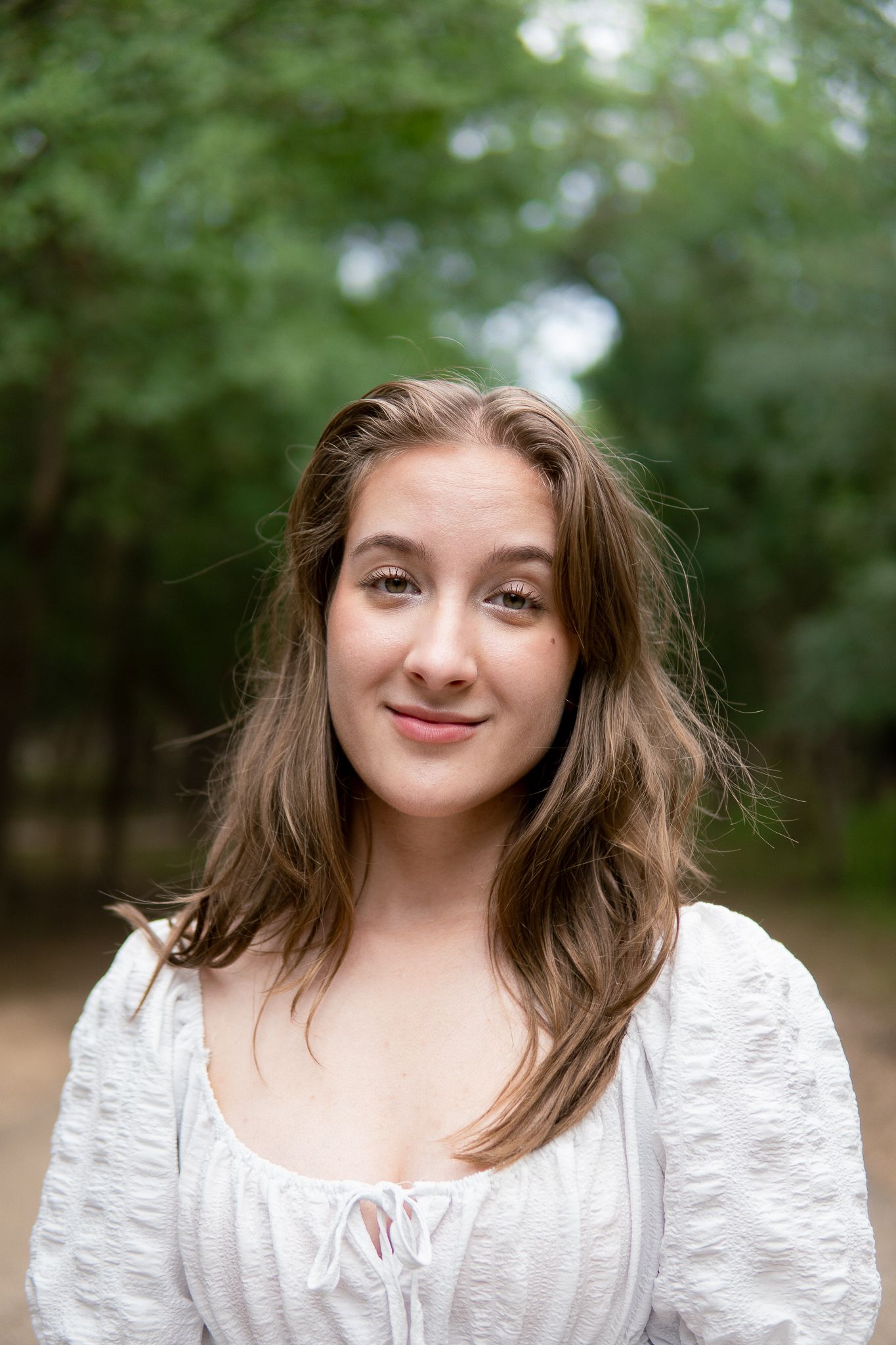 A person in a white lace dress poses outdoors against a blurred green natural background.