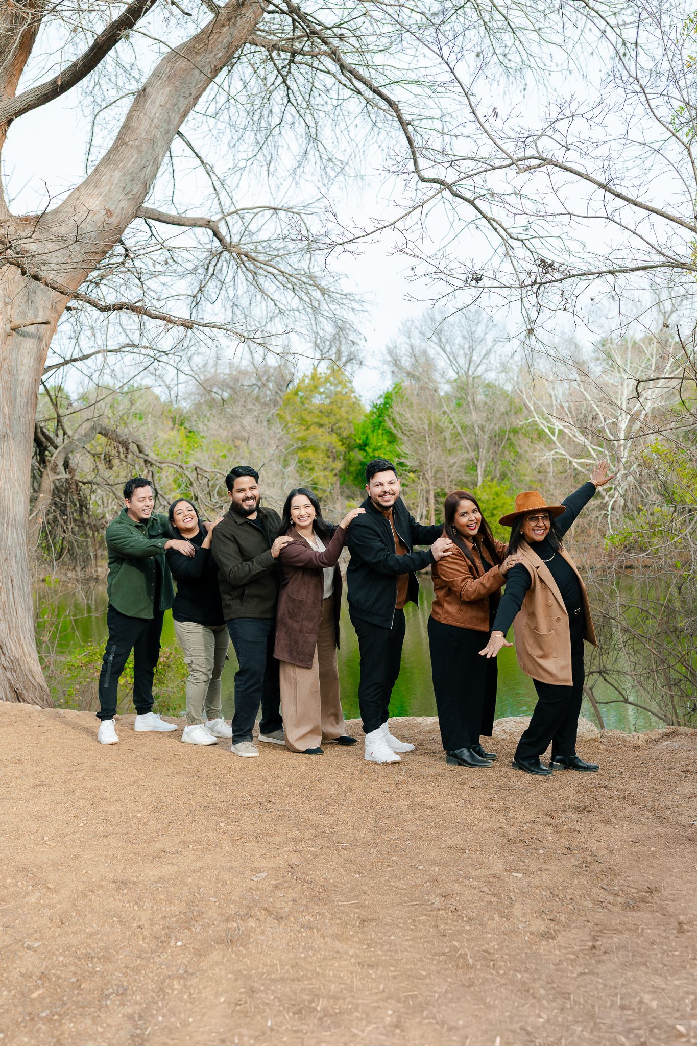 A group of people pose playfully in a line on a dirt hill against a backdrop of bare winter trees.