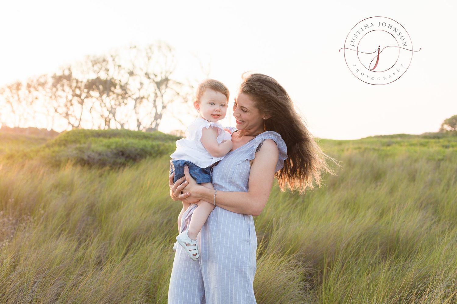 A sweet candid portrait of a parent and child embracing in tall grass during golden hour.