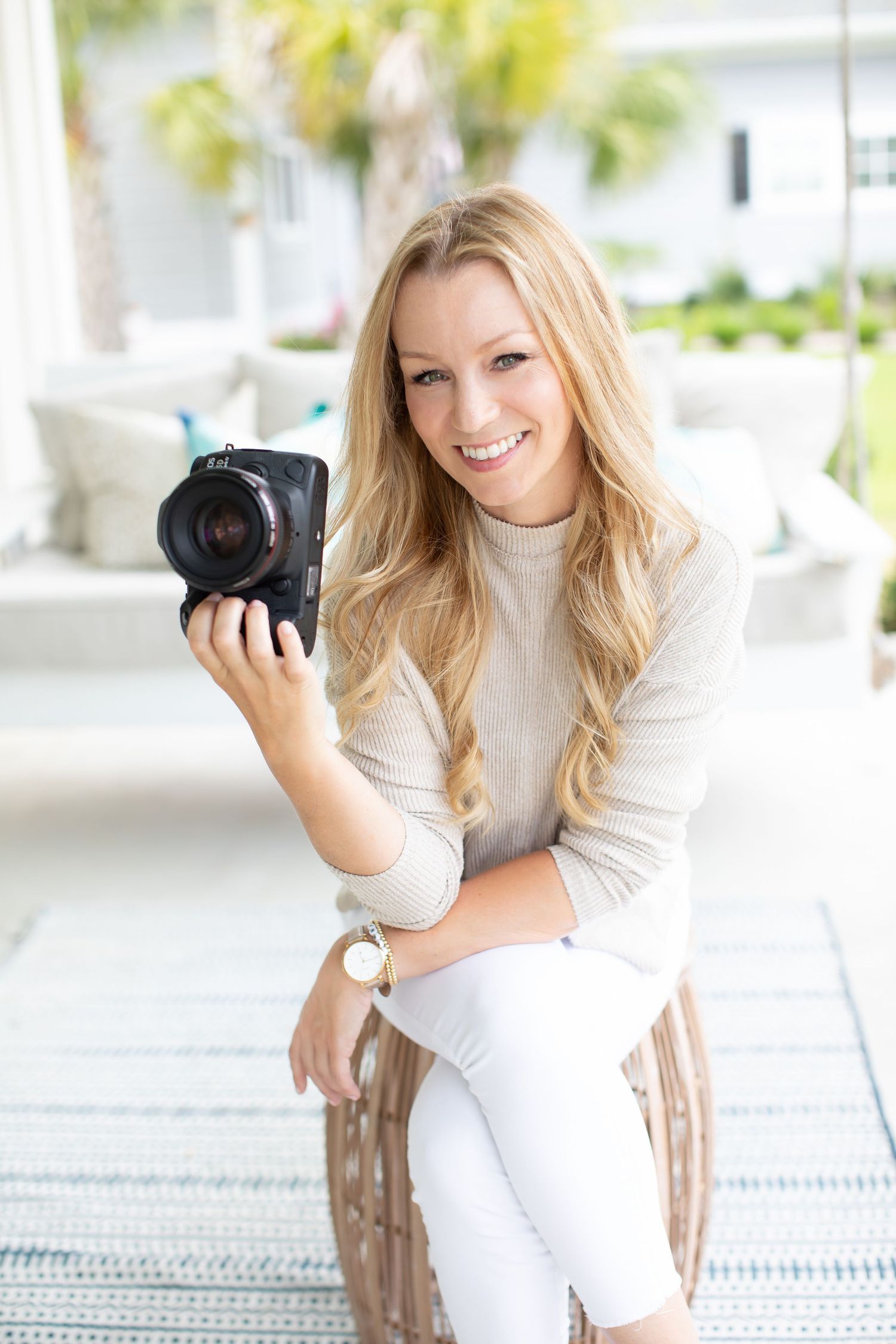 Professional photographer with camera seated in bright white coastal-style interior.