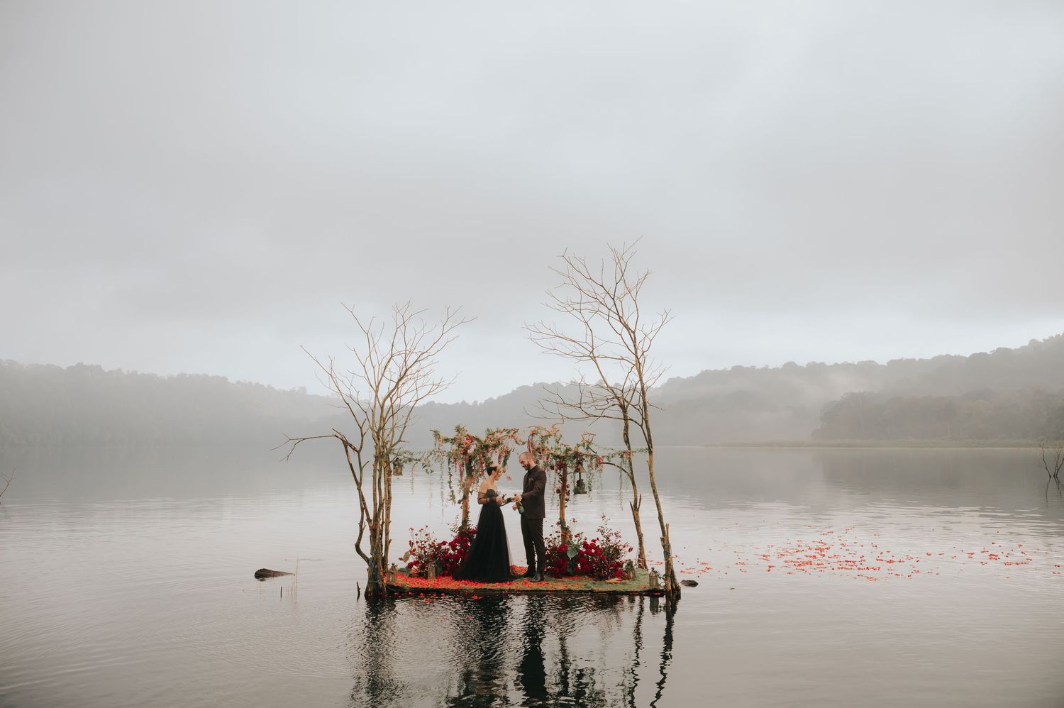 Ethereal wedding setup on lake platform with floral arrangements and scattered rose petals.