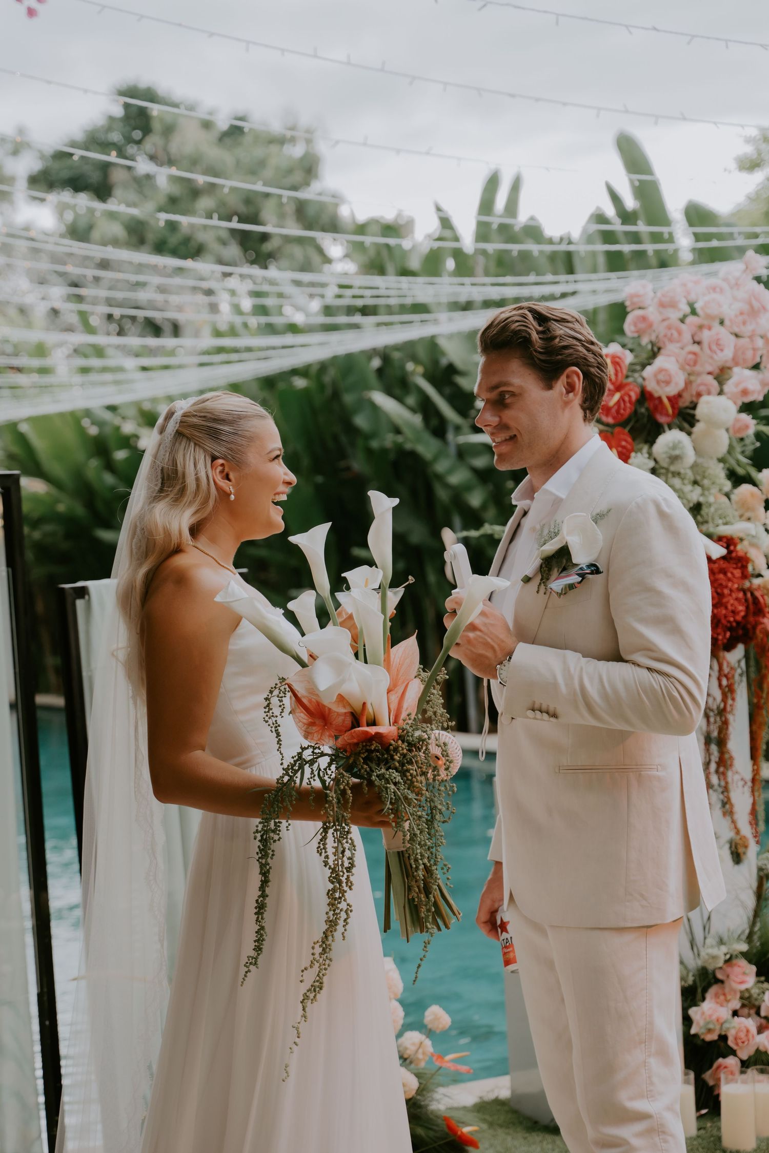 Bride and groom exchange vows at tropical outdoor wedding ceremony near pool.