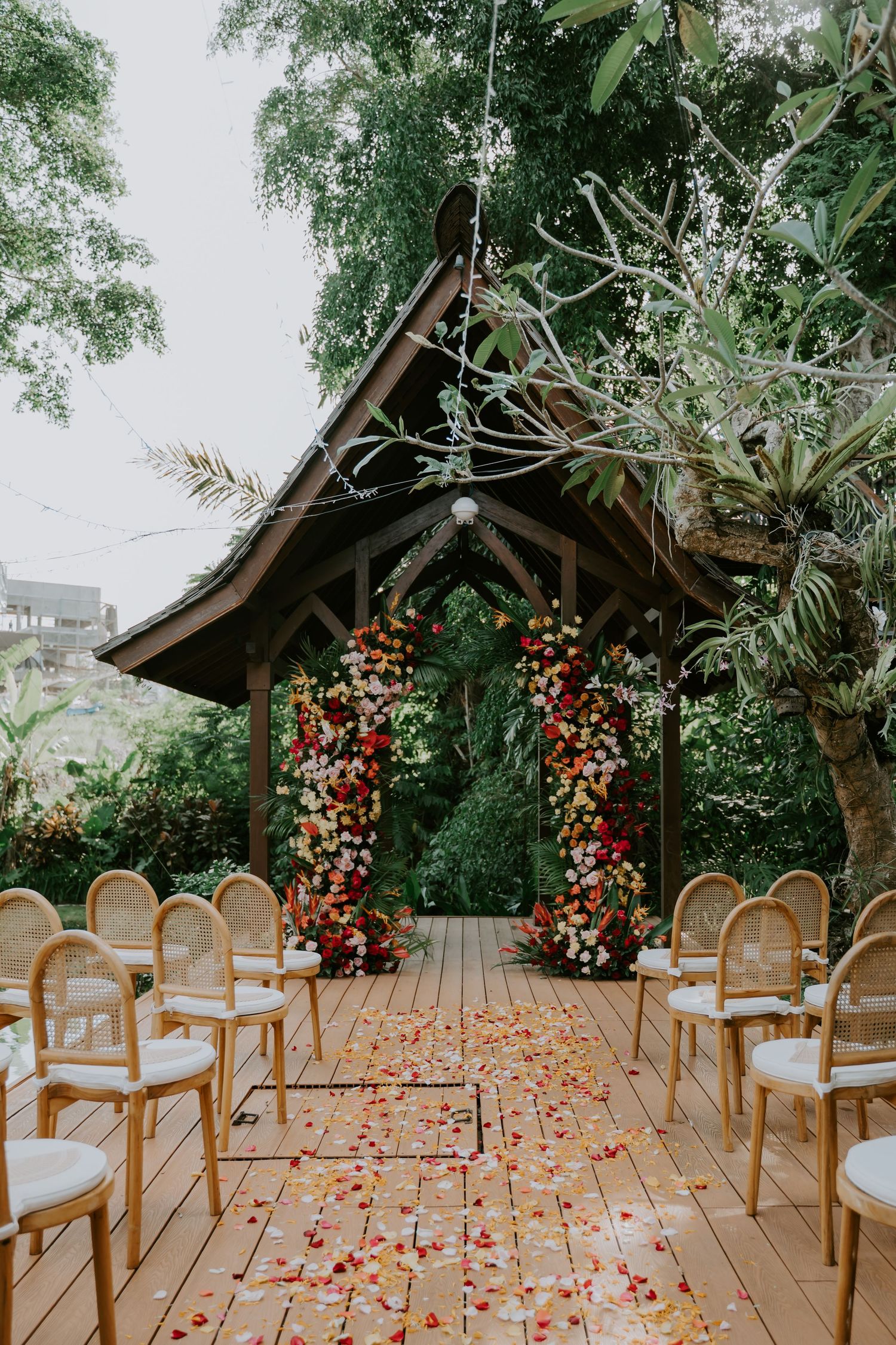 Outdoor Bali wedding ceremony venue with floral arch columns and rose petal aisle under wooden pavilion.