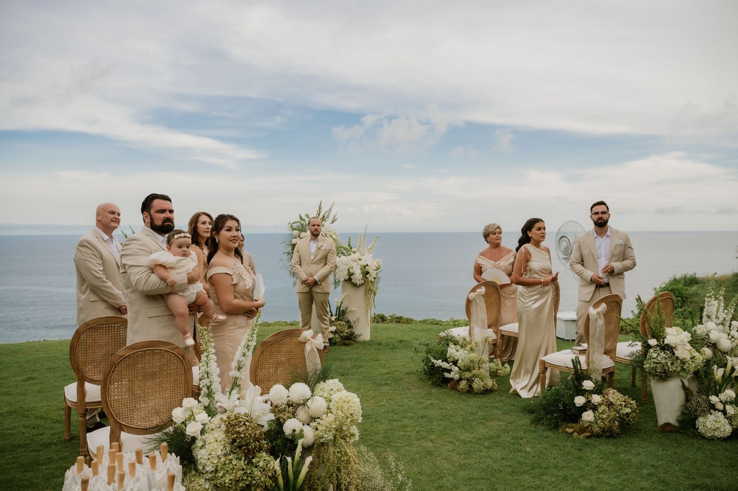 A wedding ceremony on a cliffside lawn overlooking the ocean with floral arrangements.