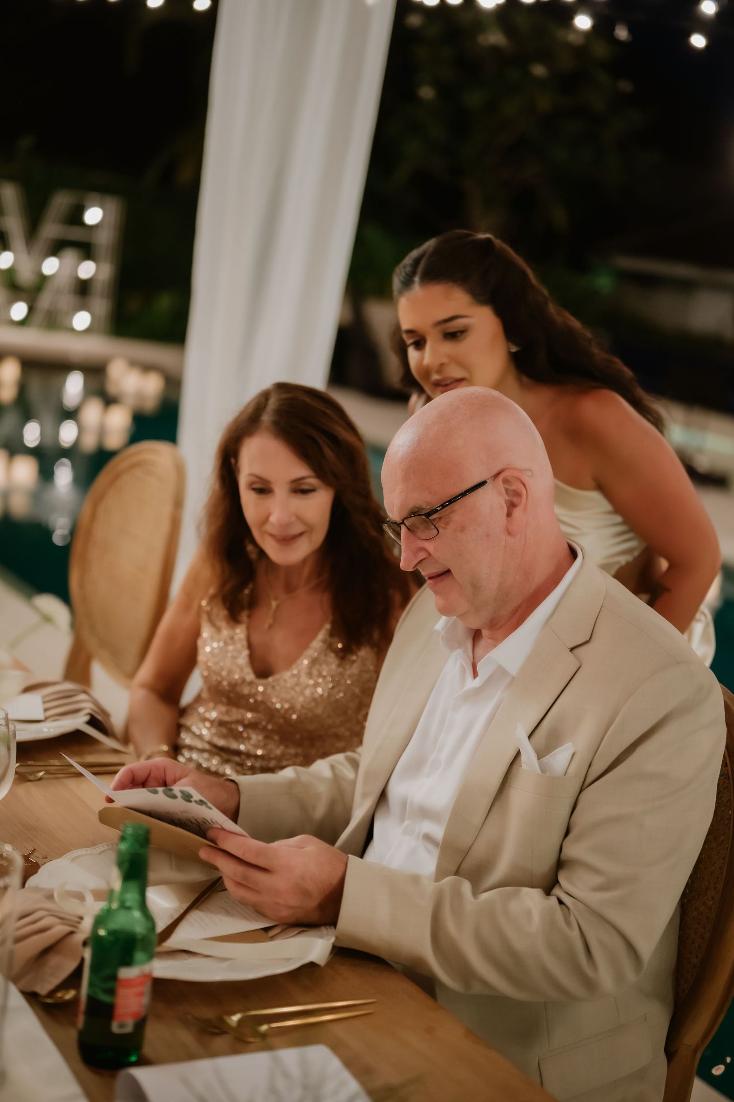 Elderly couple and young woman in evening wear reviewing photos at an elegant outdoor wedding reception dinner.