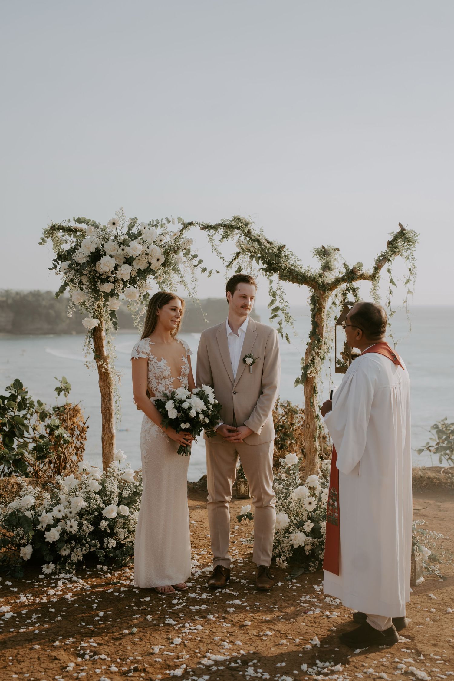 Intimate beach wedding ceremony taking place at sunset with floral arch and ocean backdrop.