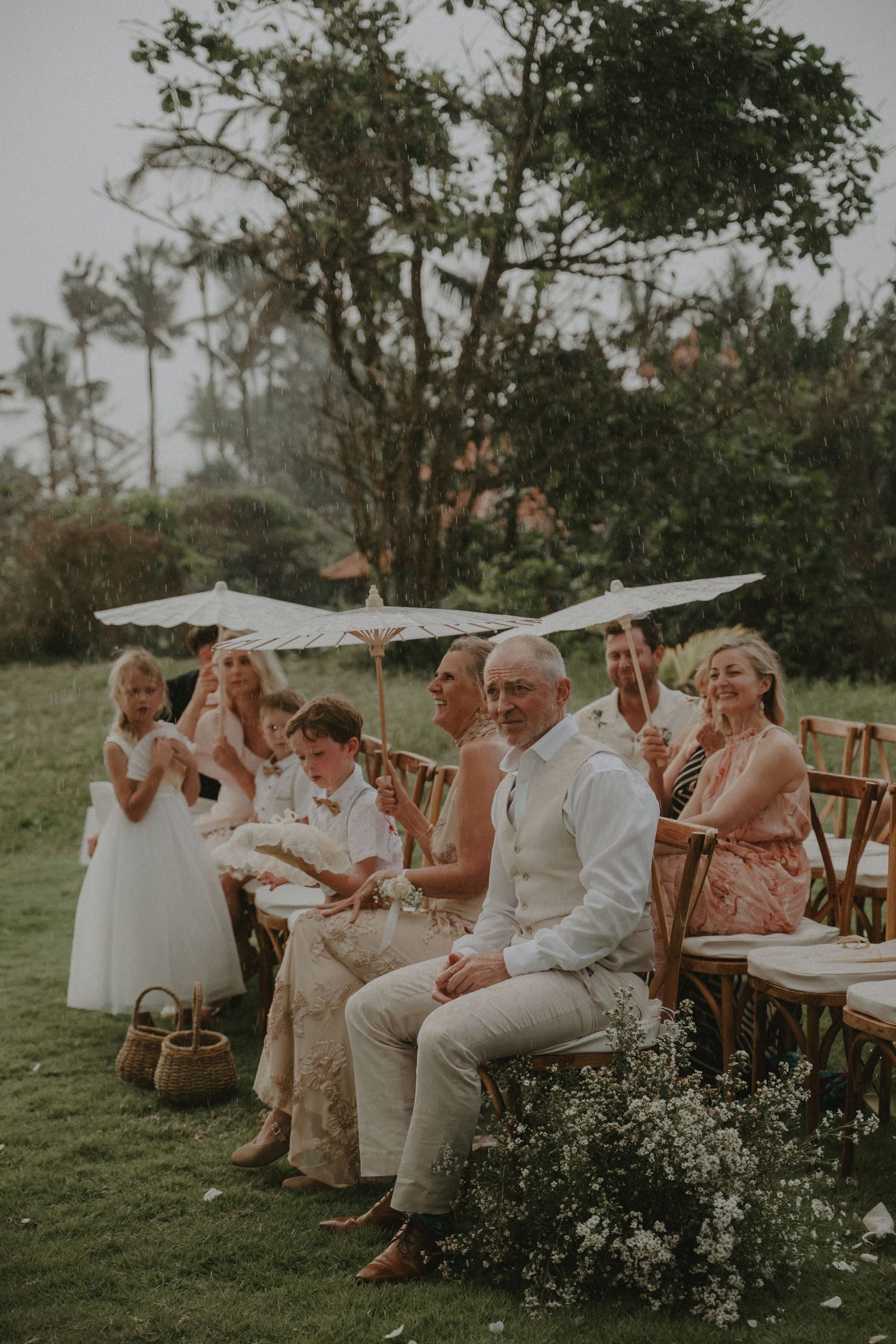 Wedding guests seated outdoors in white chairs clap and celebrate during an intimate garden ceremony.
