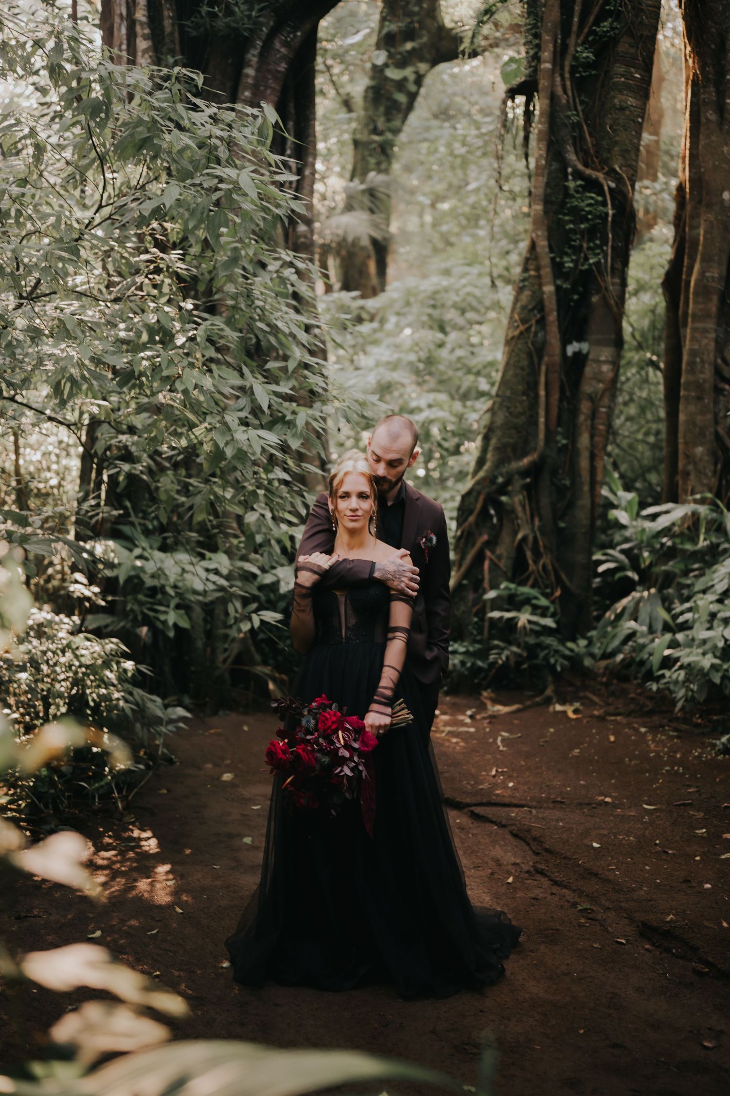 A romantic woodland photoshoot featuring a couple in dark attire surrounded by lush greenery and forest scenery.