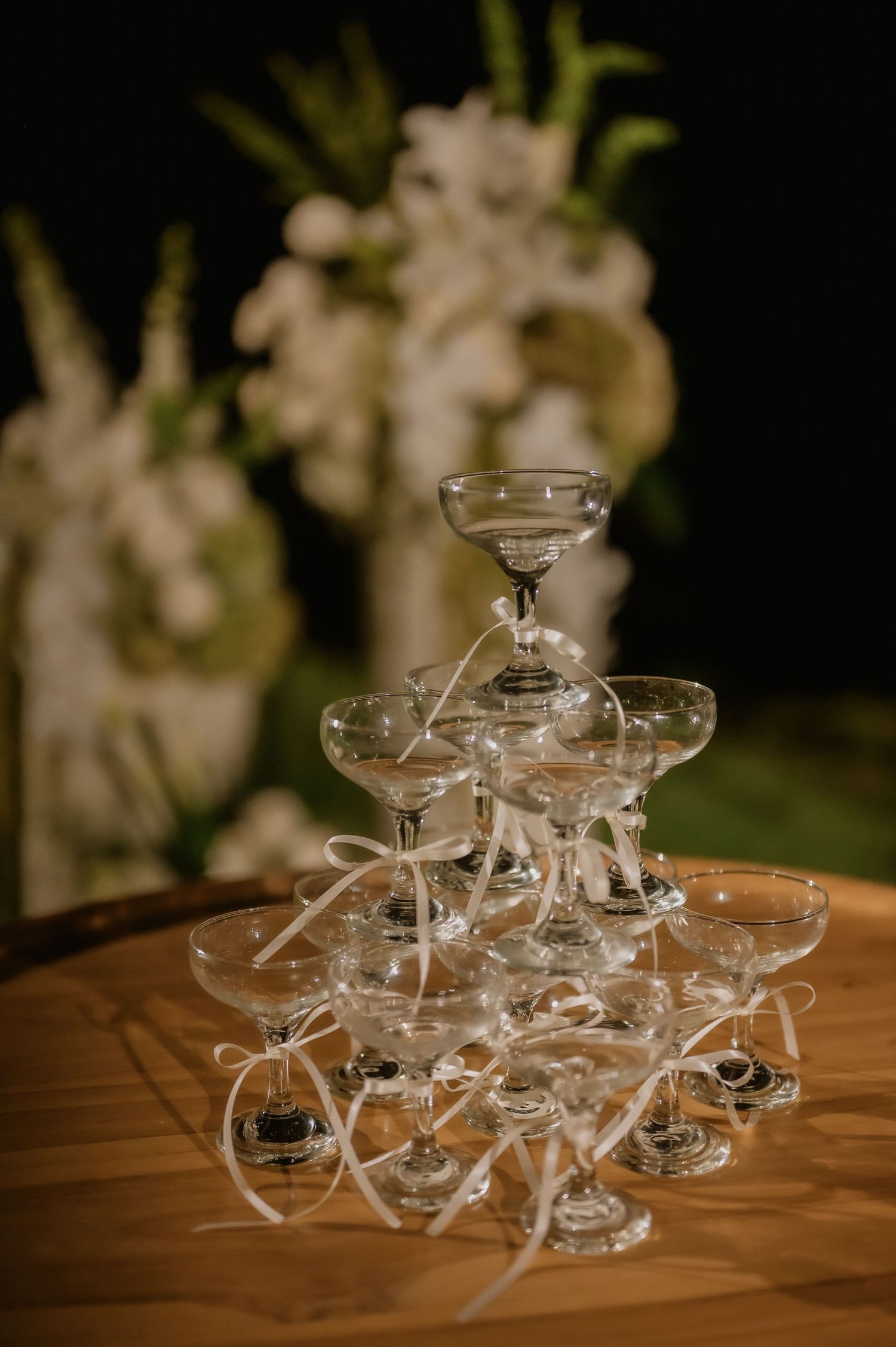 Pyramid tower of champagne coupe glasses with white ribbons at elegant wedding reception.