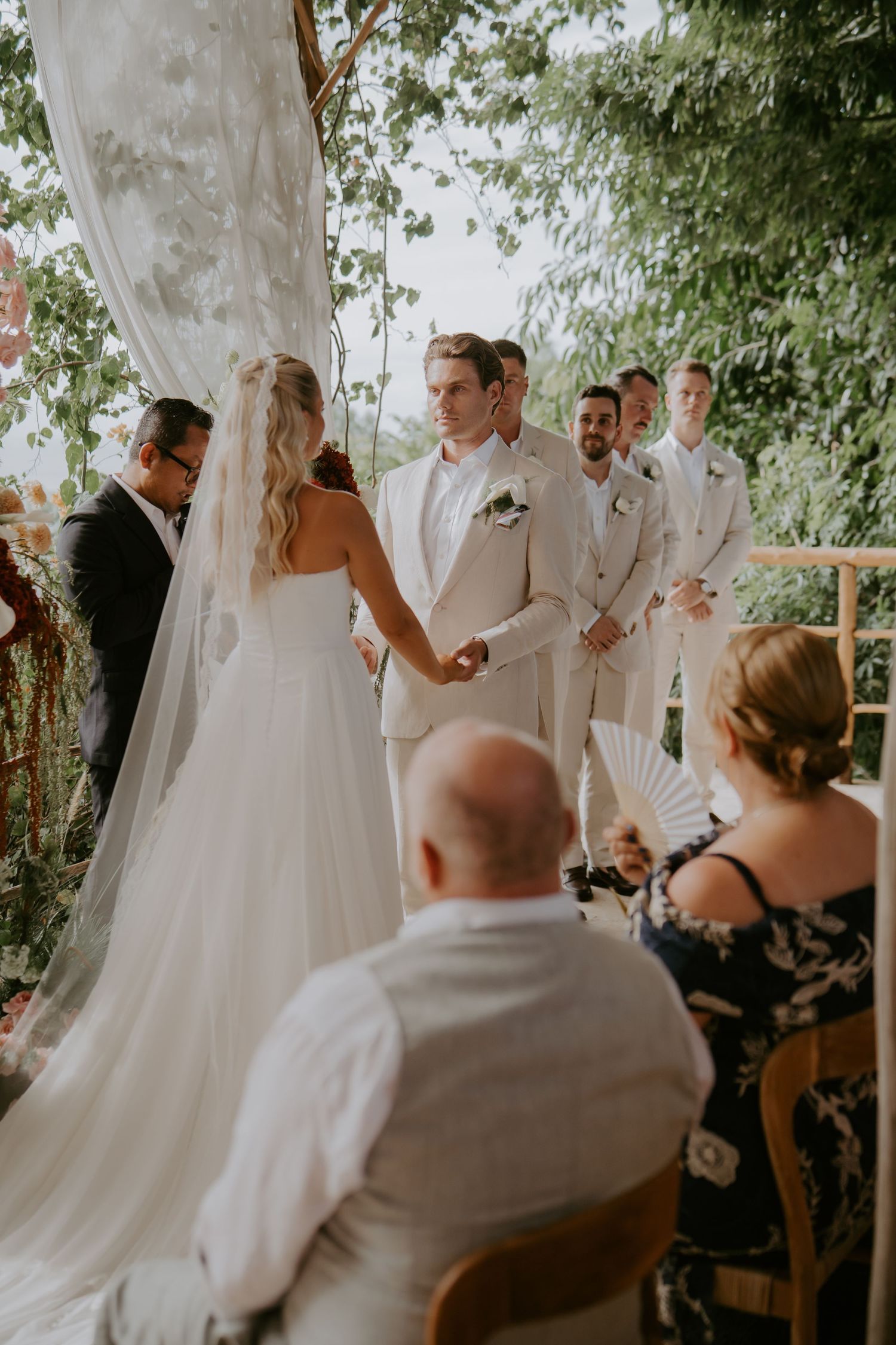 Bride and groom holding hands at an outdoor garden wedding ceremony with groomsmen.