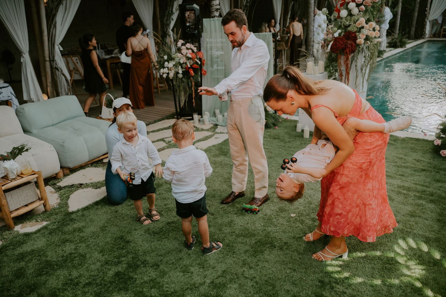 Groom and guest playfully interact with young children at tropical wedding reception.