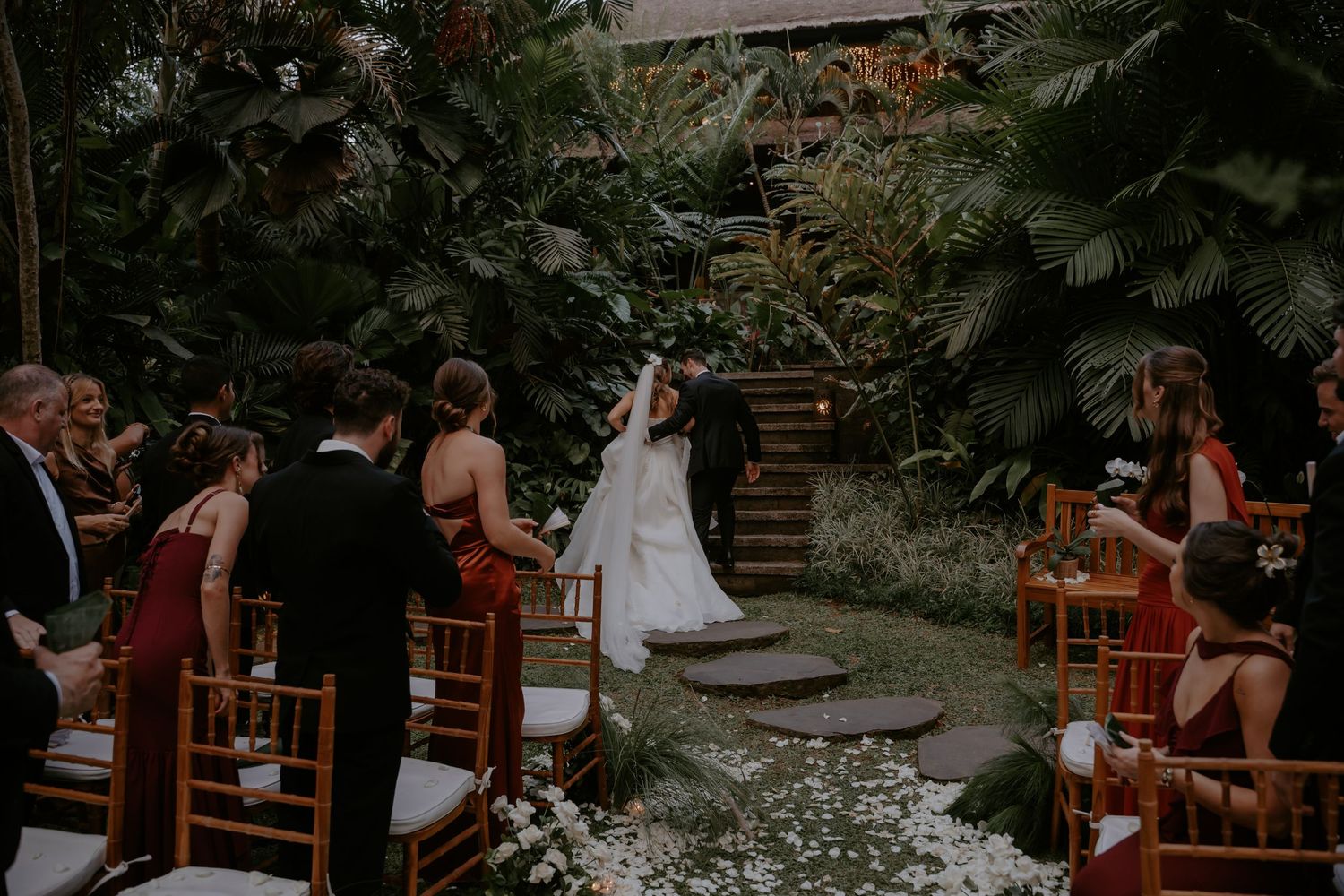 Outdoor wedding ceremony setup with wooden chairs and tropical greenery decorations.