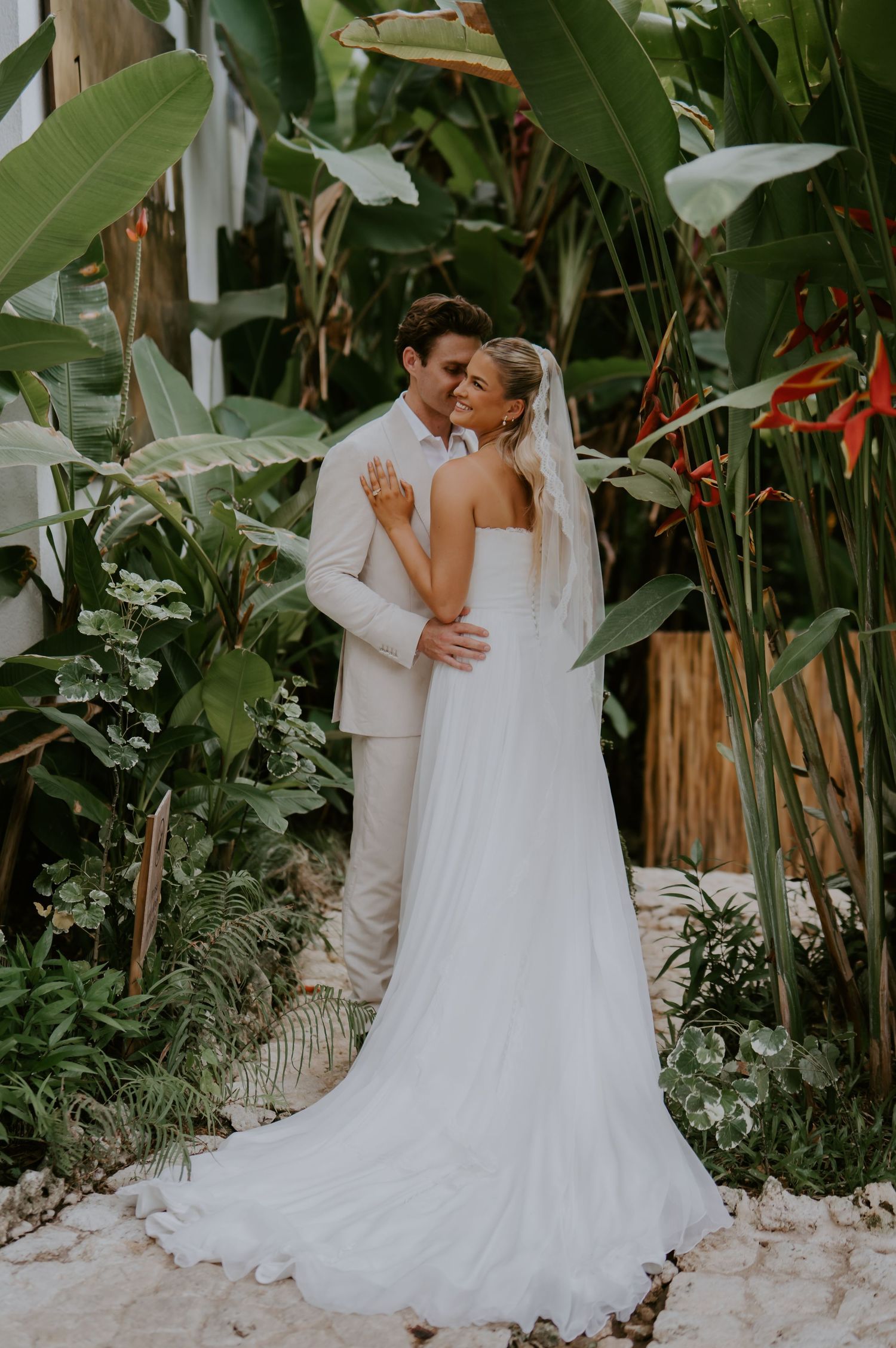 Newlywed couple embraces for romantic portrait surrounded by vibrant tropical foliage and plants.