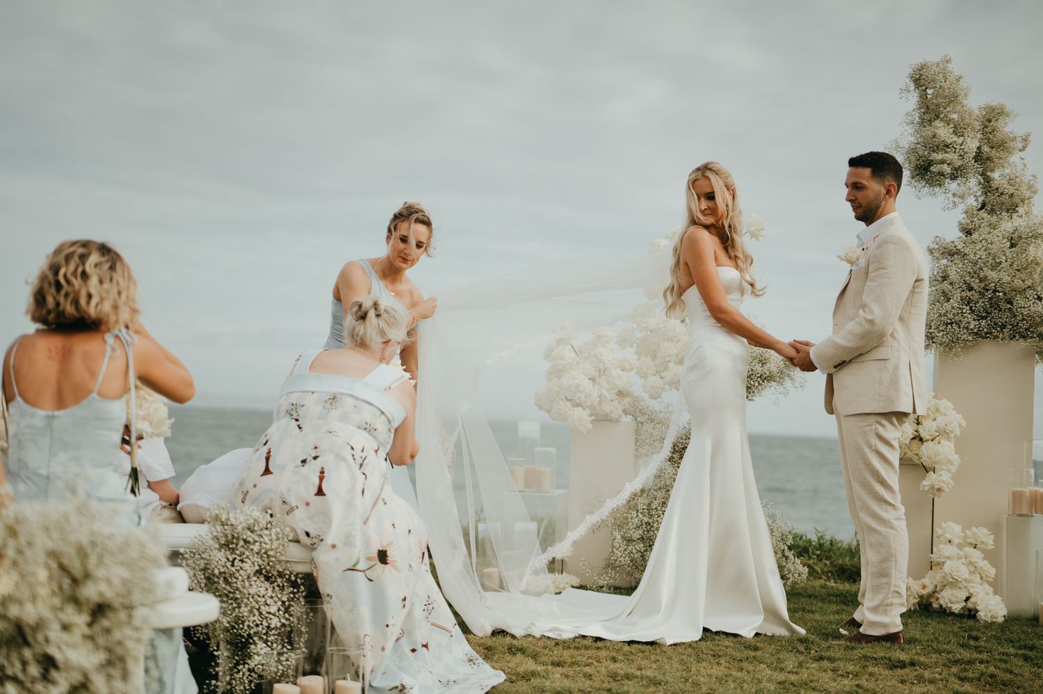 Bride and groom exchange vows at an oceanside ceremony with white floral arrangements.