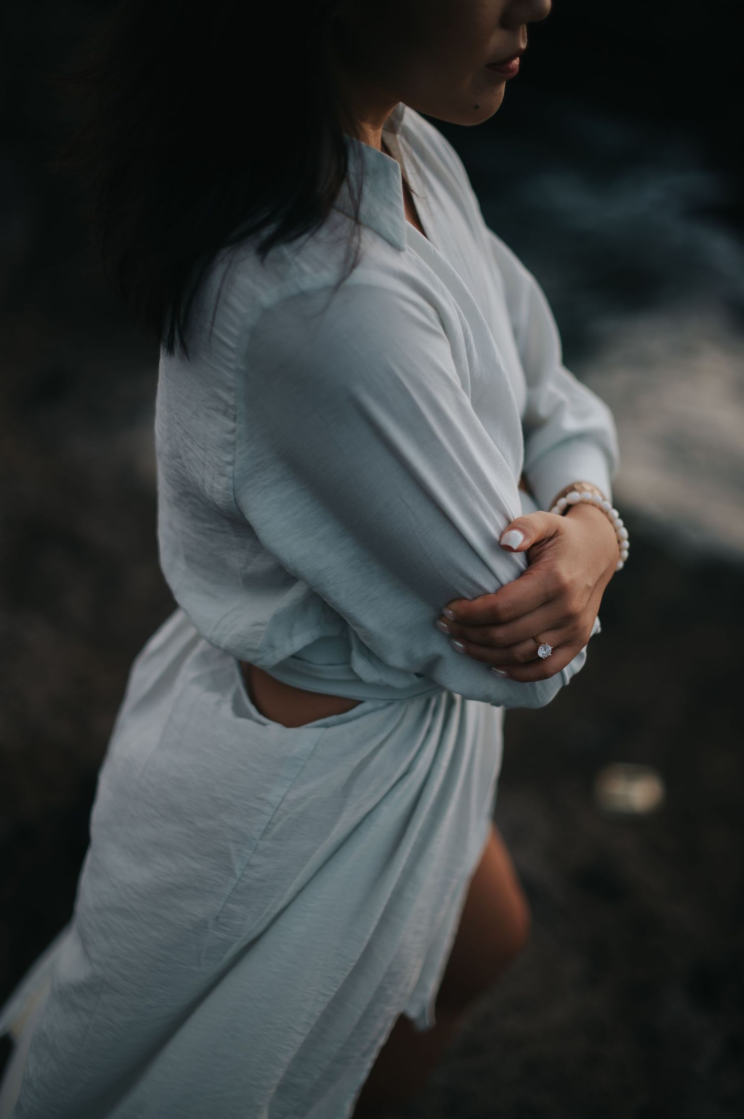Artistic maternity photo series showing woman in white dress cradling baby bump against dark background.