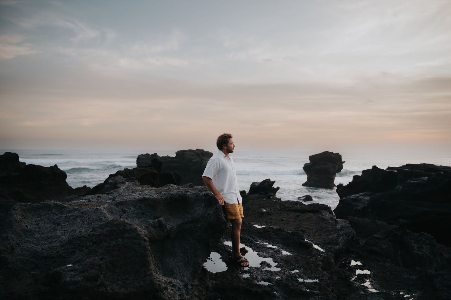 Silhouettes of people walking along rocky coastline during dramatic sunset with waves crashing against cliffs.