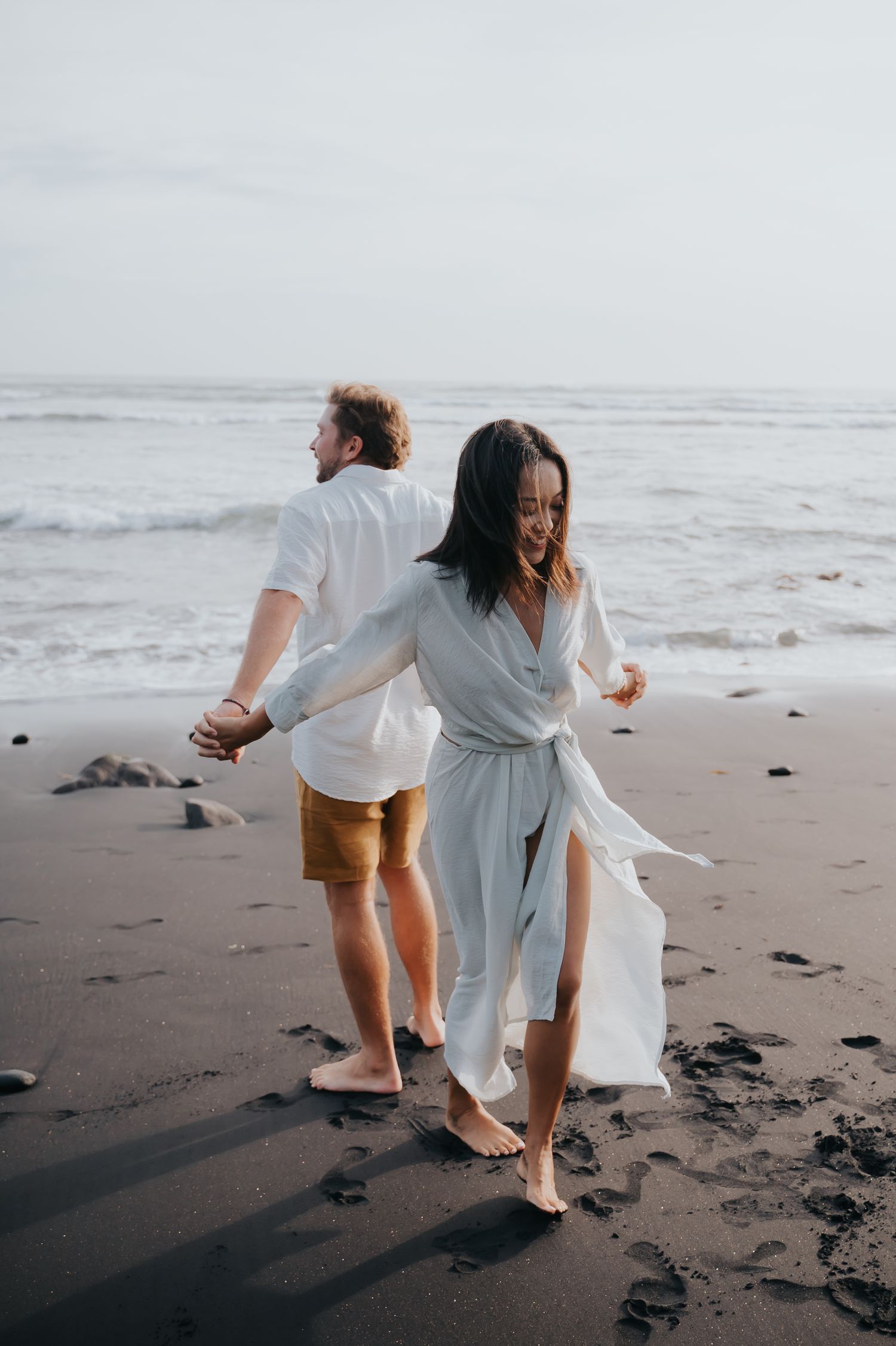 Couple walking playfully together on a misty black sand beach near the ocean waves.