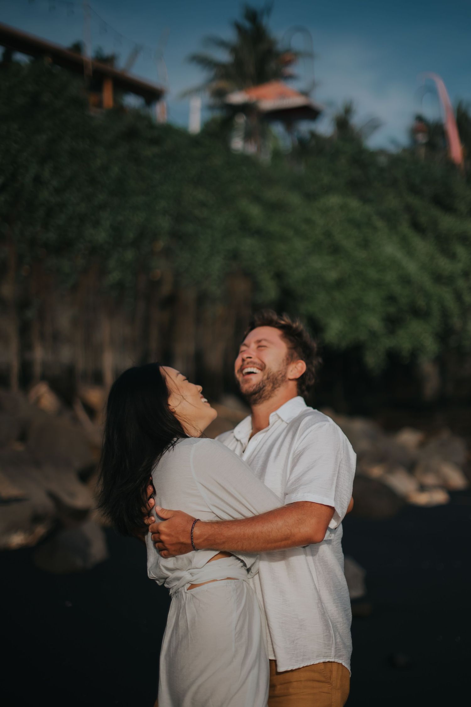 A couple shares a joyful embrace outdoors against a green natural backdrop during golden hour.