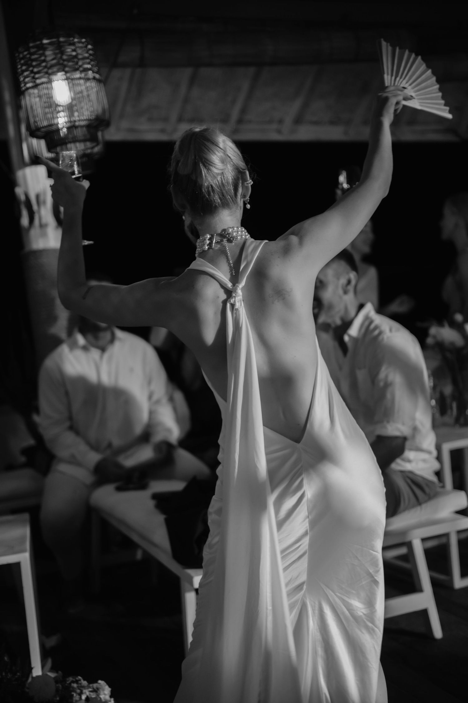 Elegant bride in backless white gown raises her arm while dancing at reception.