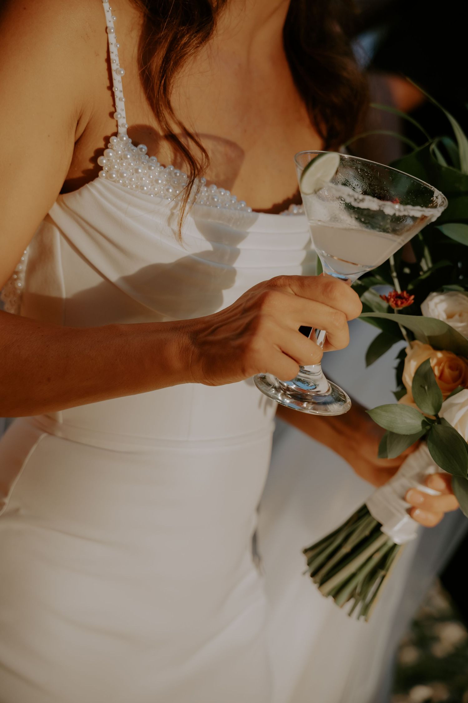 Close-up detail shots of a bride in a white wedding dress holding a floral bouquet with greenery.