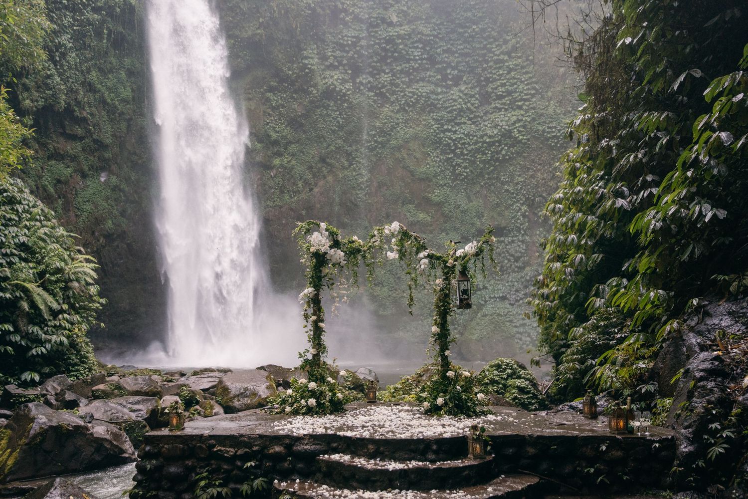 A panoramic view of a majestic waterfall cascading down a lush green cliff surrounded by tropical vegetation.