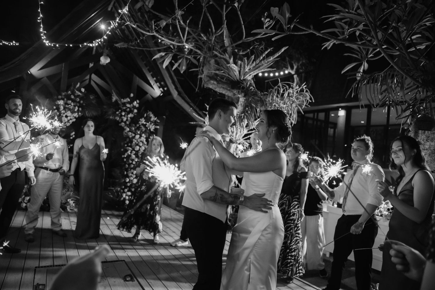 Black and white photo of newlyweds sharing first dance surrounded by sparklers at night.