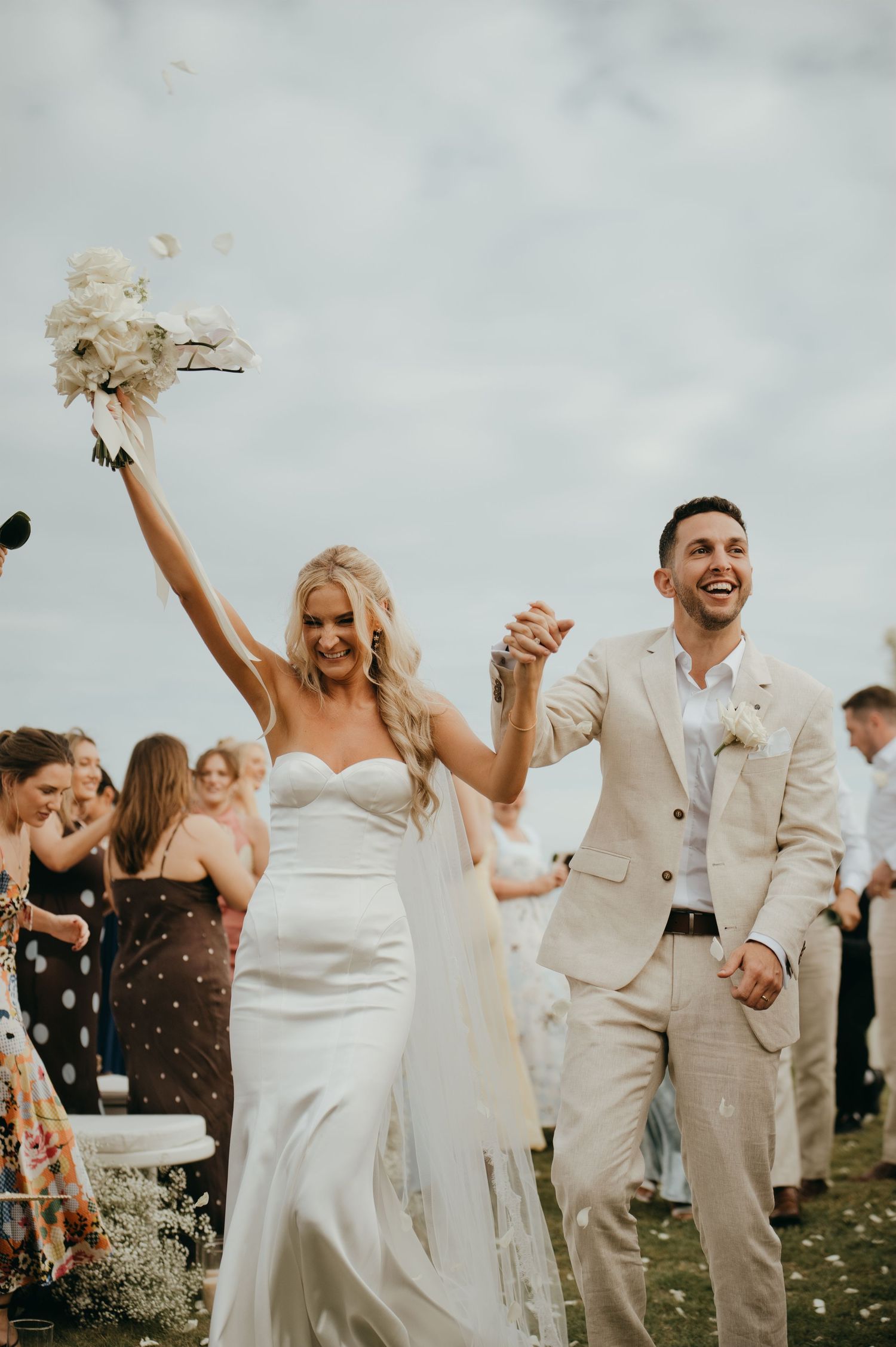 Joyful newlyweds walk back down the aisle as guests celebrate with confetti at an outdoor wedding.