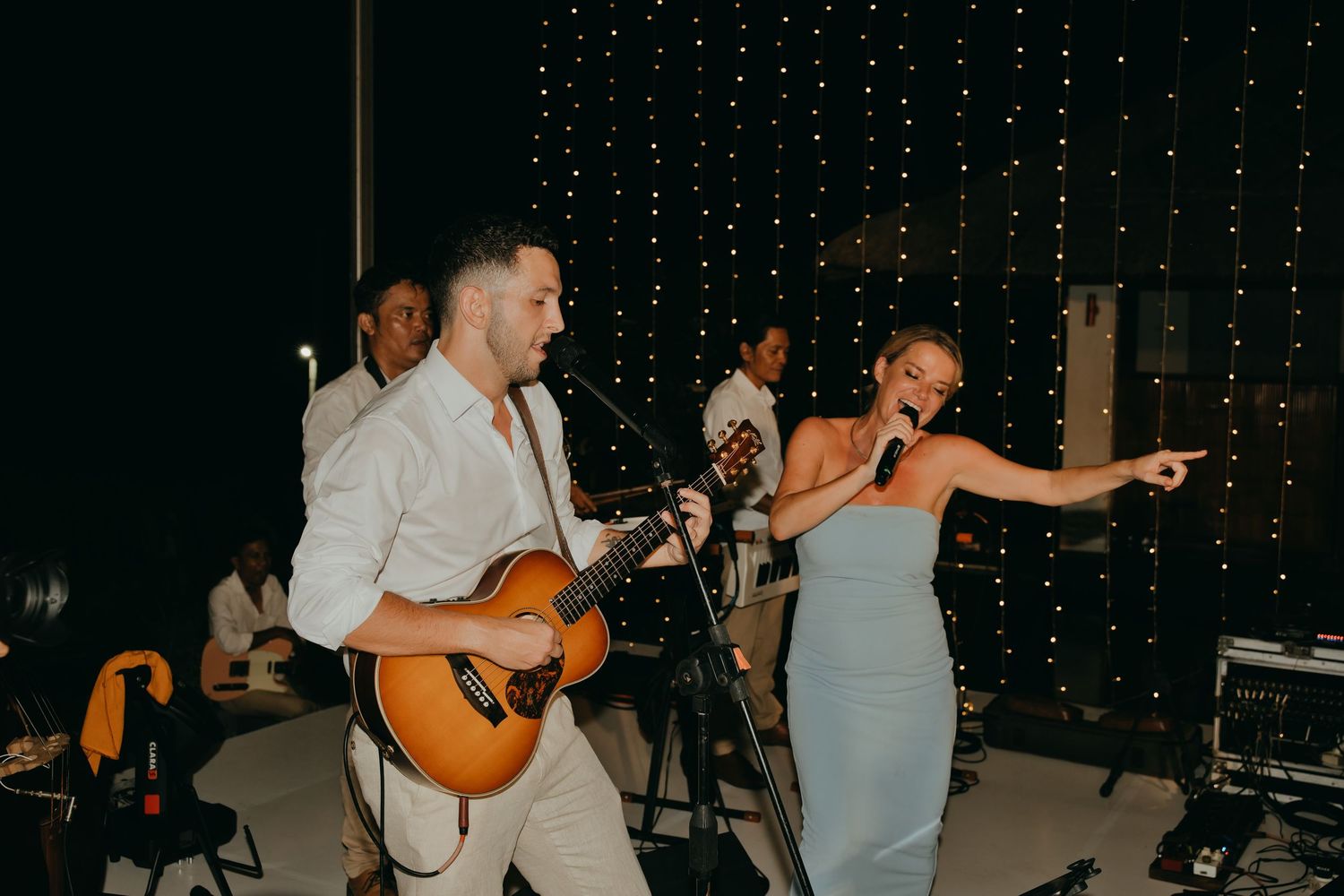 Live band performs at wedding reception with guitarist and female singer in blue dress entertaining guests.
