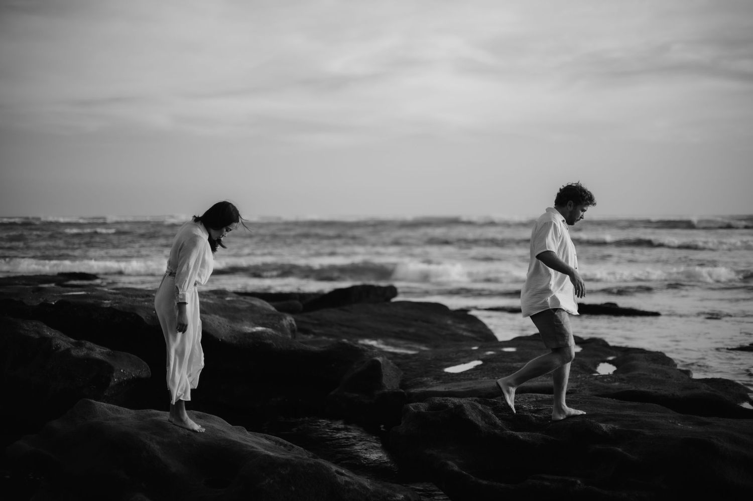 Seven black and white photographs show silhouettes of figures walking along a moody beach at sunset.