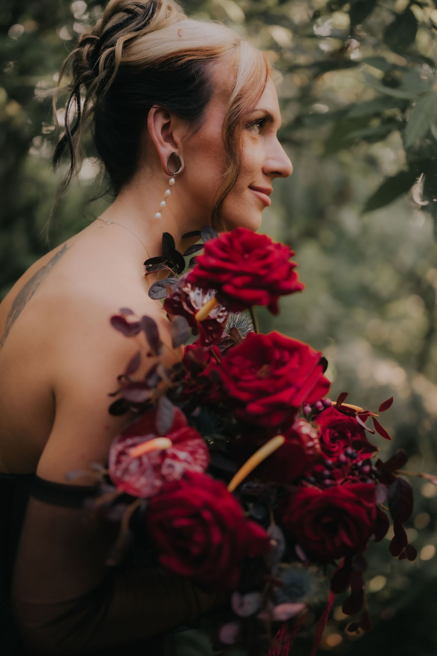 Close-up of burgundy rose bouquet with dark foliage held by someone in a black dress.