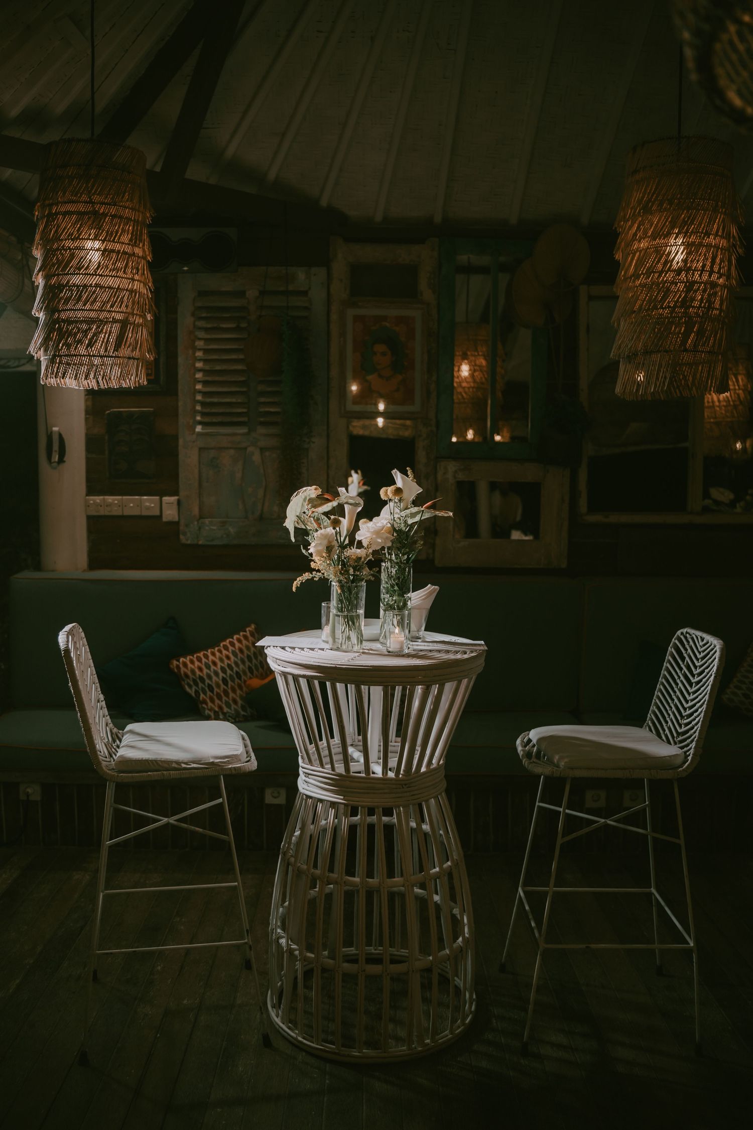 Moody interior of restaurant with rattan pendant lights and white table settings.
