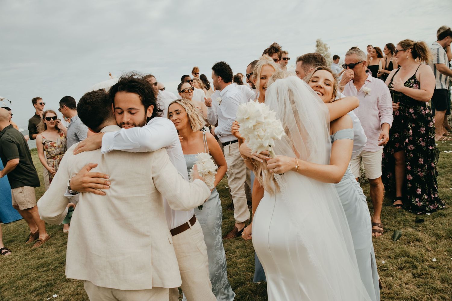 Newlyweds and guests celebrate joyfully after the outdoor wedding ceremony with hugs and laughter.