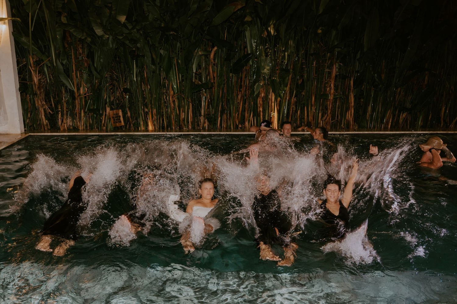 Wedding guests splashing feet in pool at night during outdoor reception celebration.