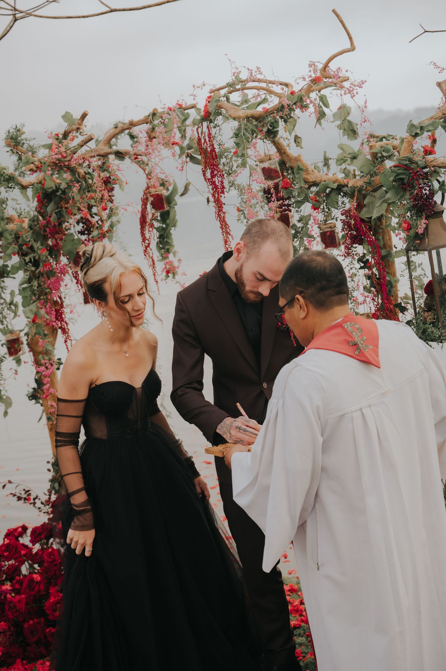 A wedding ceremony in progress under a floral arch with red and white blooms.