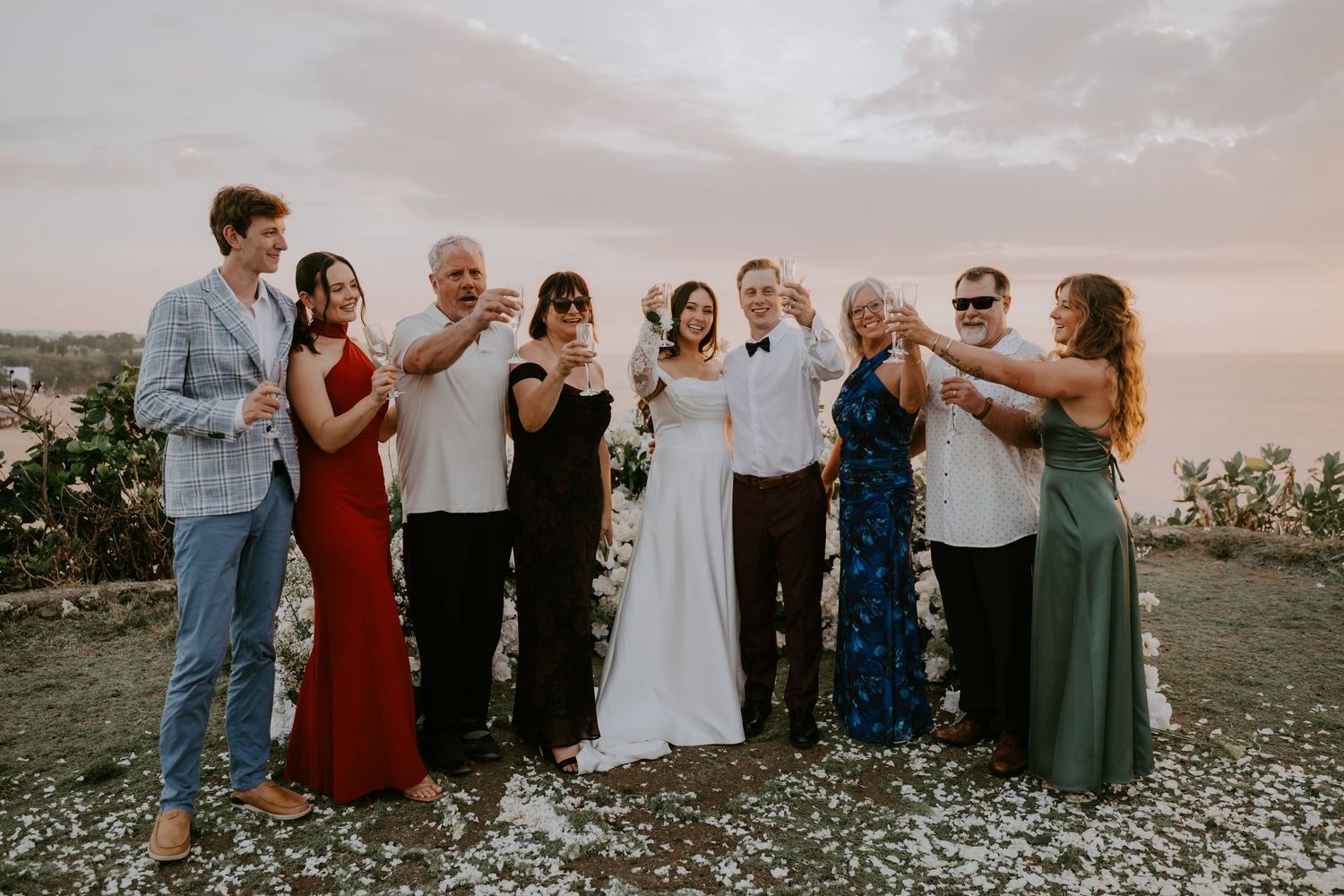 Wedding party group toast celebration with ocean sunset backdrop outdoors.