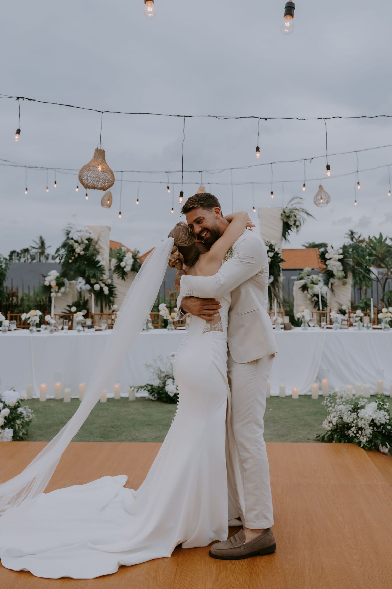Newlyweds share first dance embrace under string lights at elegant outdoor wedding reception.
