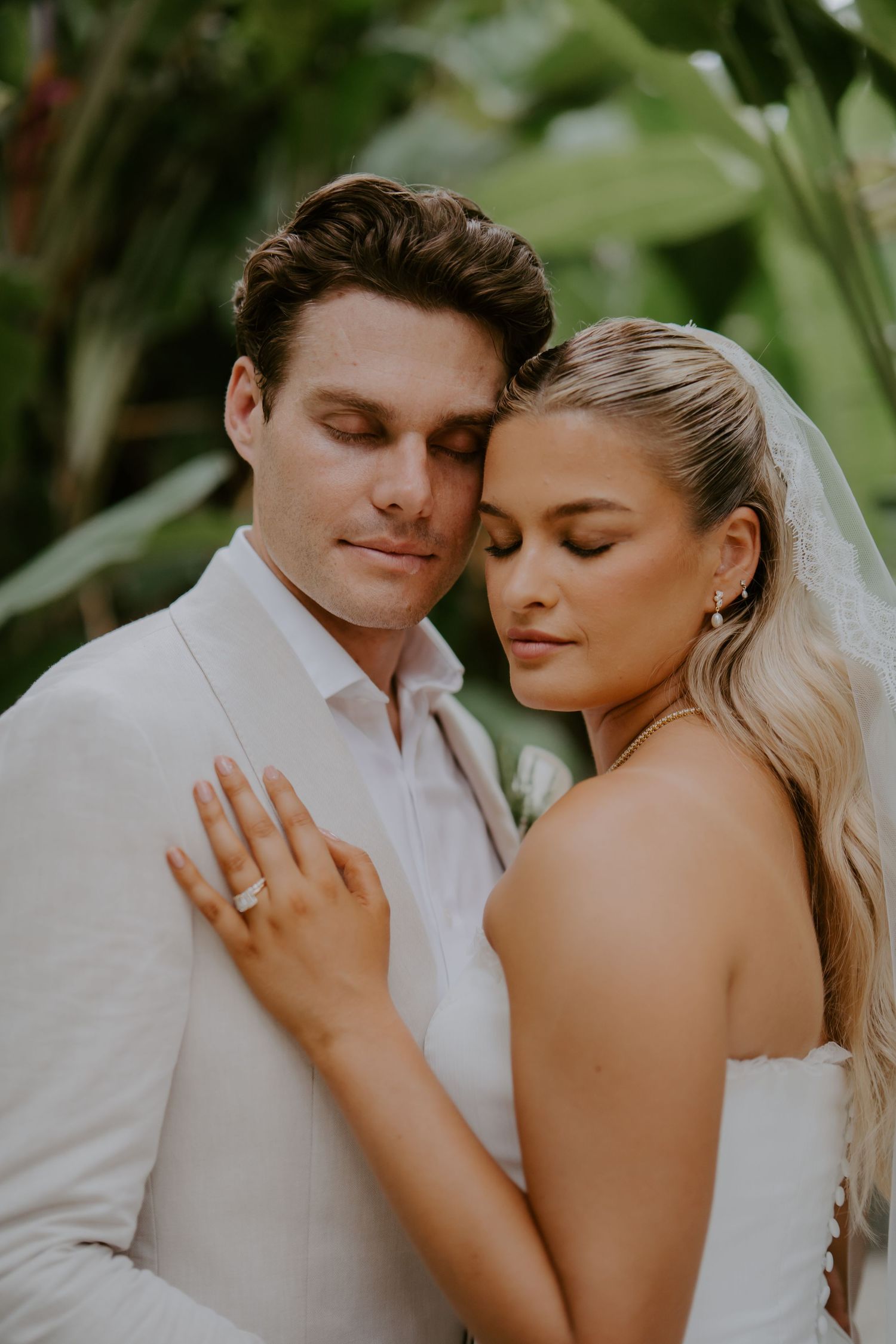 Bride and groom share a tender romantic moment, eyes closed, as she rests her head on his shoulder wearing a wedding veil.