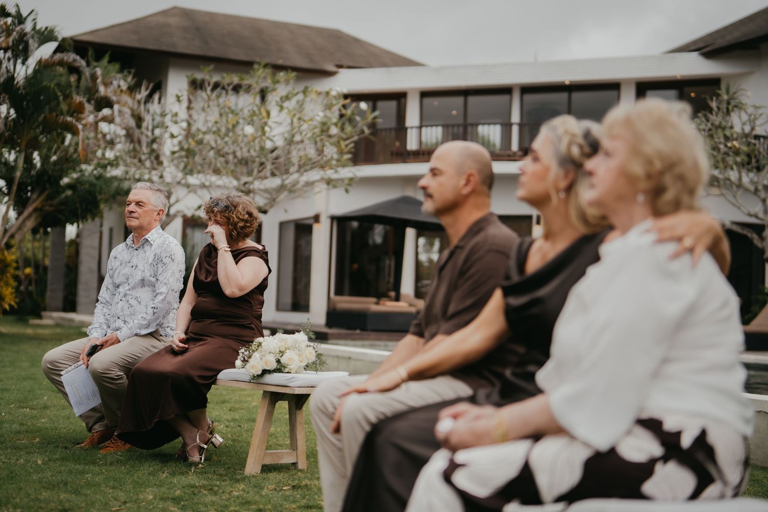 Small group of wedding guests seated on benches during outdoor garden wedding ceremony.
