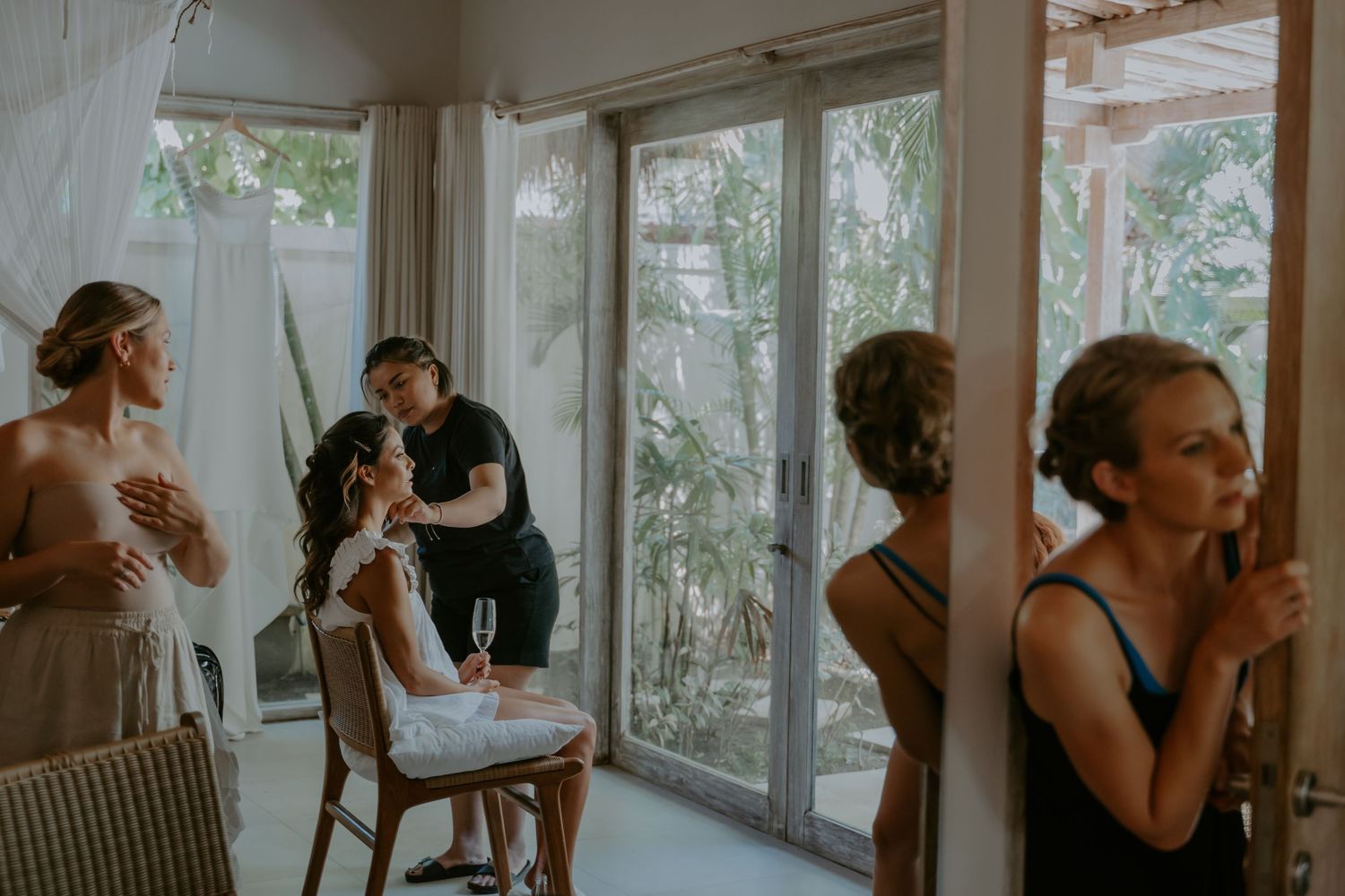 People getting ready in a sunlit room with floor-to-ceiling windows and sheer curtains during a special occasion.