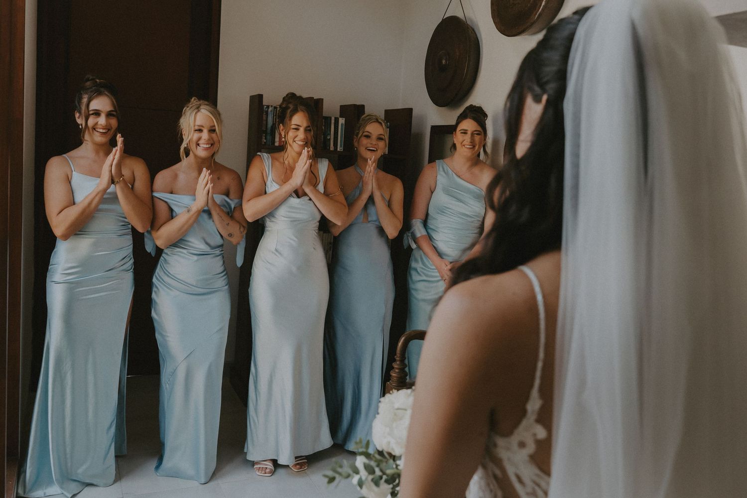 Bridesmaids in light blue dresses react emotionally during a wedding ceremony moment.