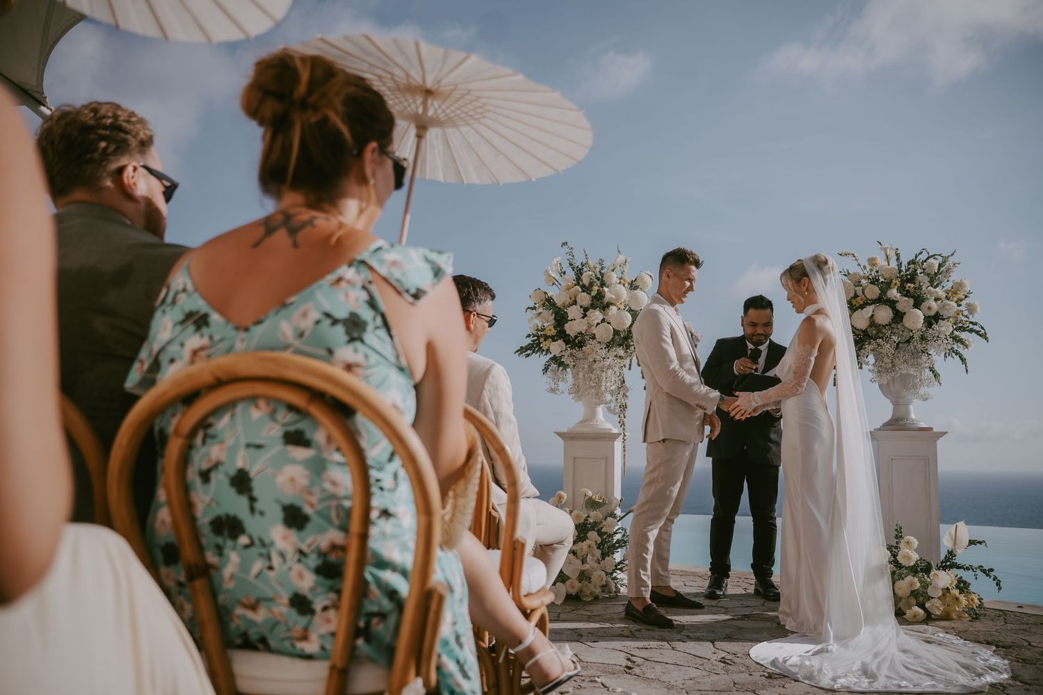 Beachside wedding ceremony setup with white parasols and floral arrangements.