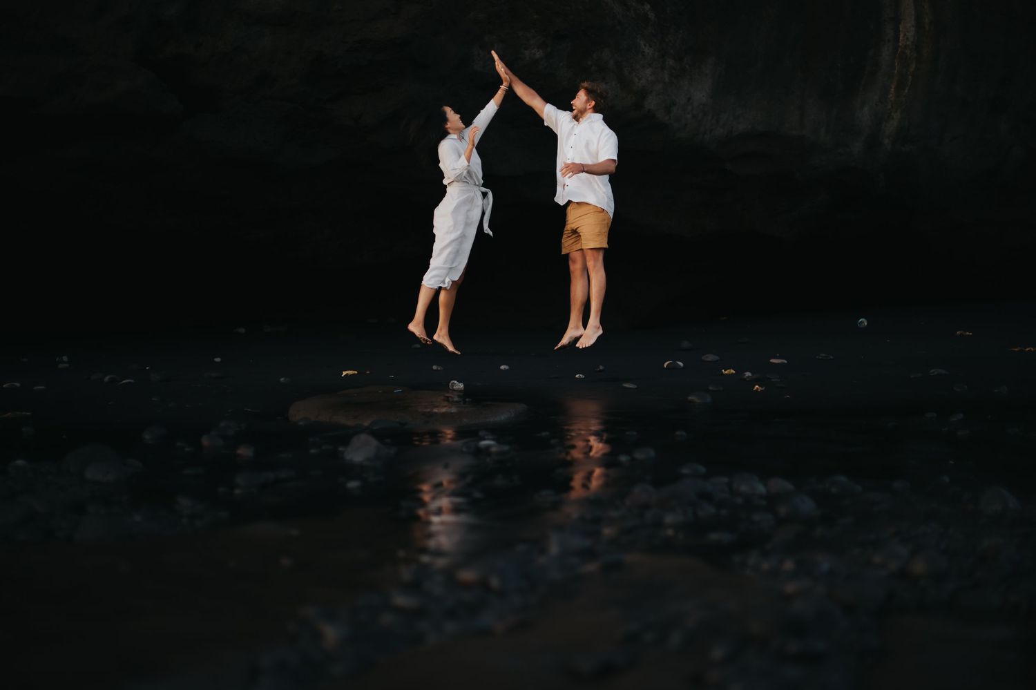 Two people stand in dark shallow water during sunset creating a silhouette against the evening sky.