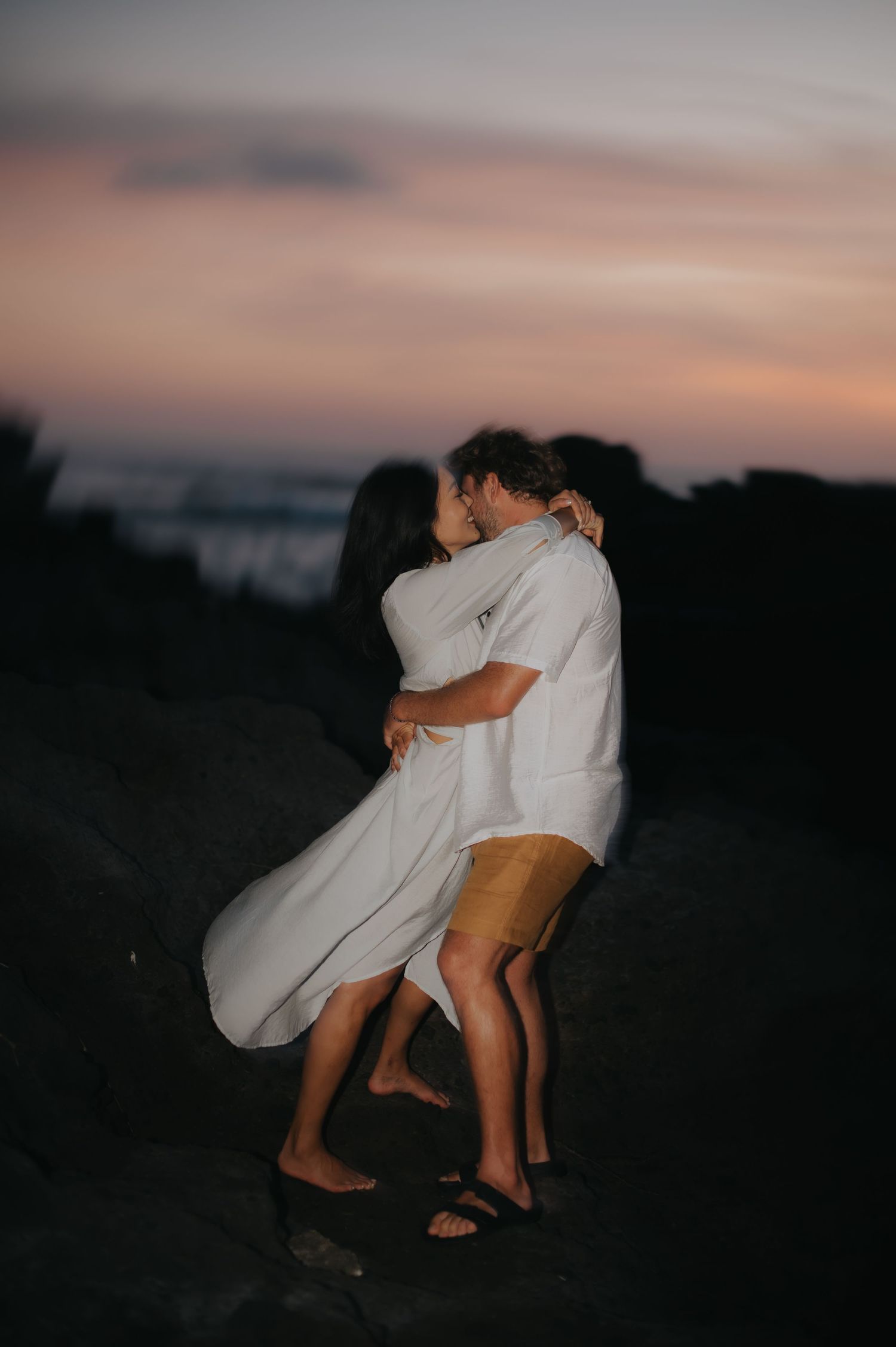 A couple in white outfits embraces during sunset in a romantic series of silhouetted poses.