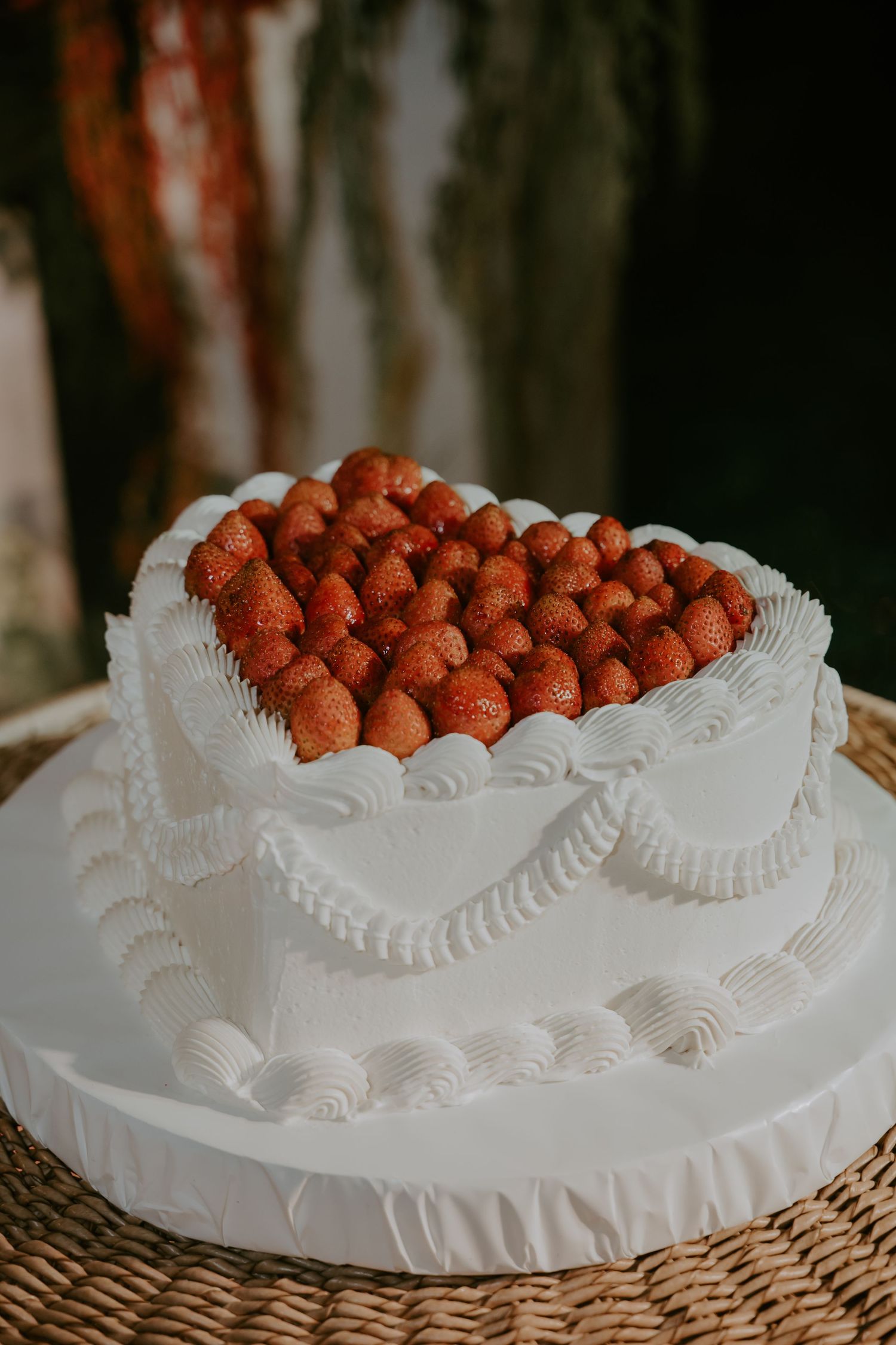 Two-tier white wedding cake topped with fresh strawberries and decorated with elegant piped frosting details.
