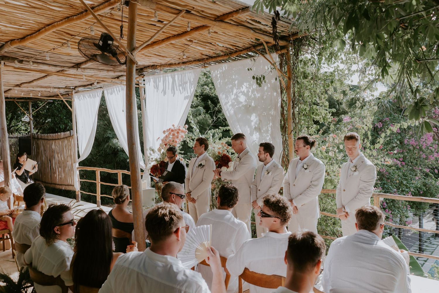 Outdoor wedding ceremony under bamboo pavilion with groom and groomsmen awaiting the bride.